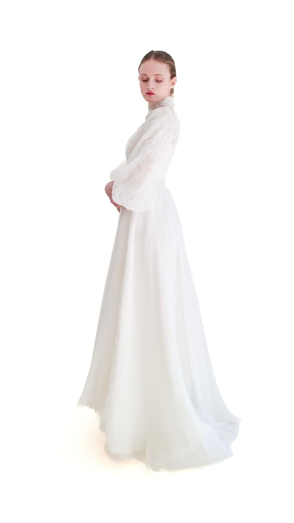 Step back in time with our 1960's Vintage Balloon Sleeve Wedding Gown. This true vintage piece features modest yet elegant long balloon sleeves, a high neck, and delicate fabric covered buttons. Perfect for a timeless and sophisticated wedding