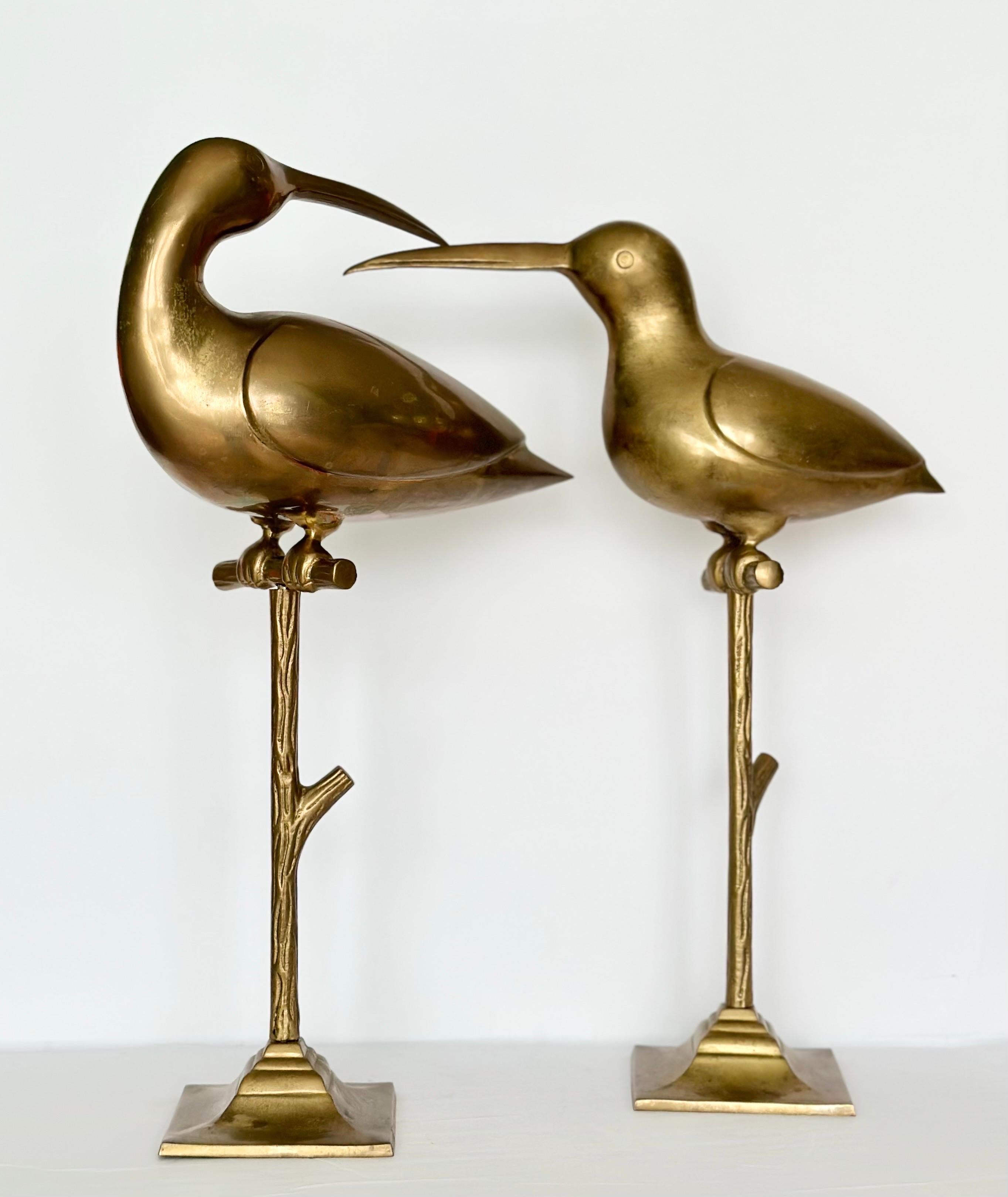 We are very pleased to offer a stunning pair of vintage figurine birds, circa the 1960s.  This captivating pair of vintage brass bird sculptures portray a graceful curlew perched upon a sturdy branch. The brass material adds a touch of timeless