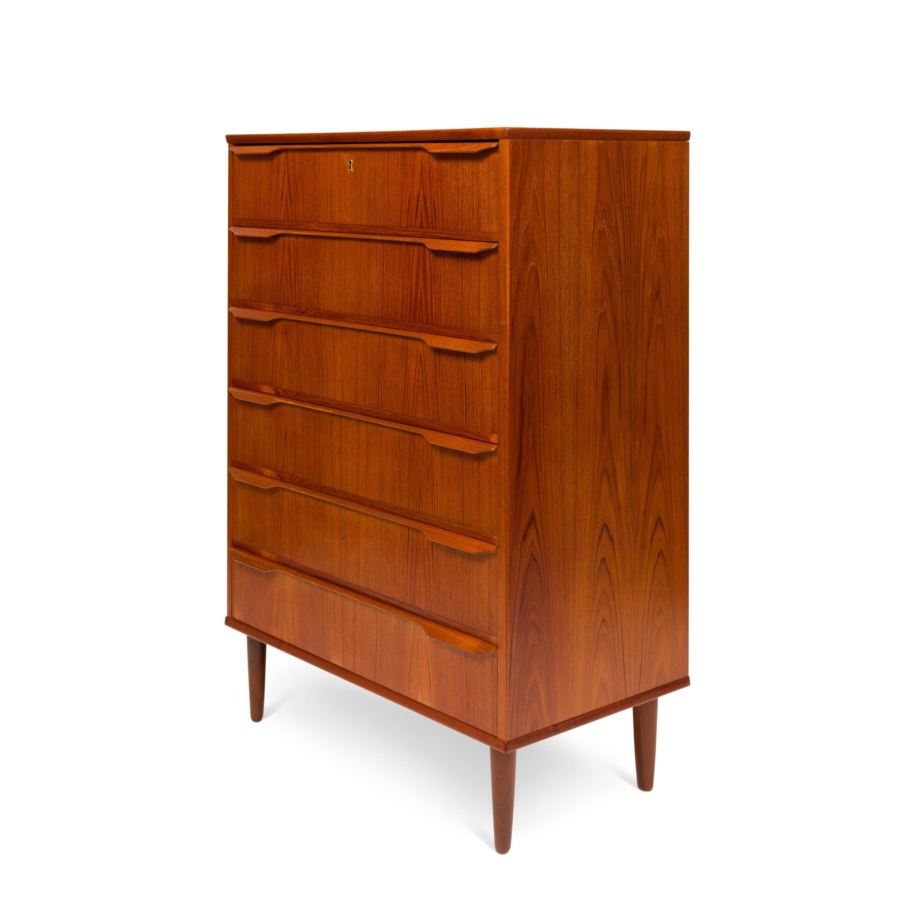 A handsome 1960s vintage Danish mid-century six-drawer teak tallboy dresser stands as an emblem of timeless design. The chest of drawers exhibits a mesmerizing teak grain, complemented by elongated sculpted drawer pulls. Its embodiment of the Danish