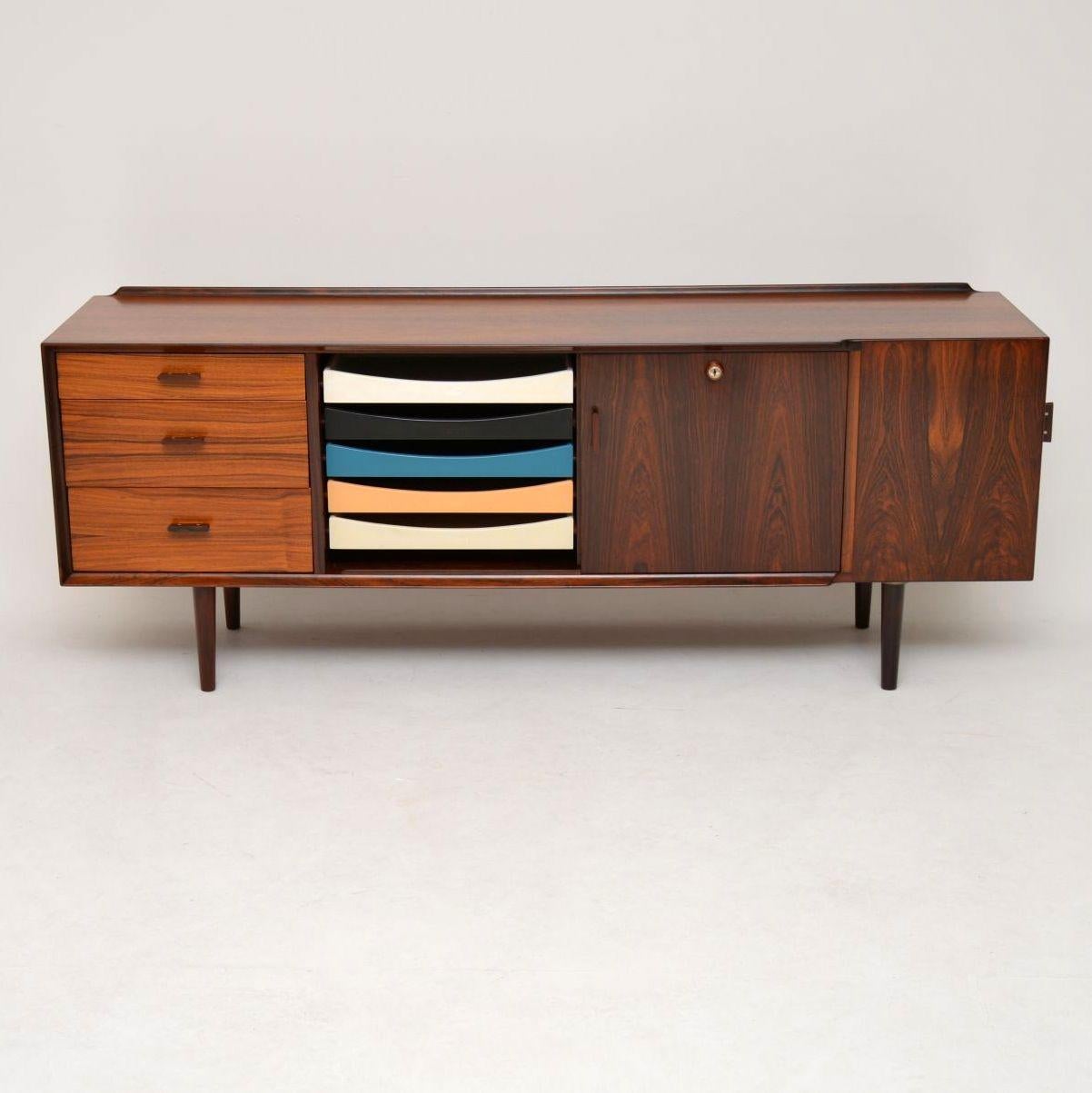 A magnificent vintage Danish sideboard, this was designed by Arne Vodder and made by Sibast in the 1960s. It has colourful slide out tray drawers in the middle, with drawers and a cabinet on either side, there is also another built in cabinet that