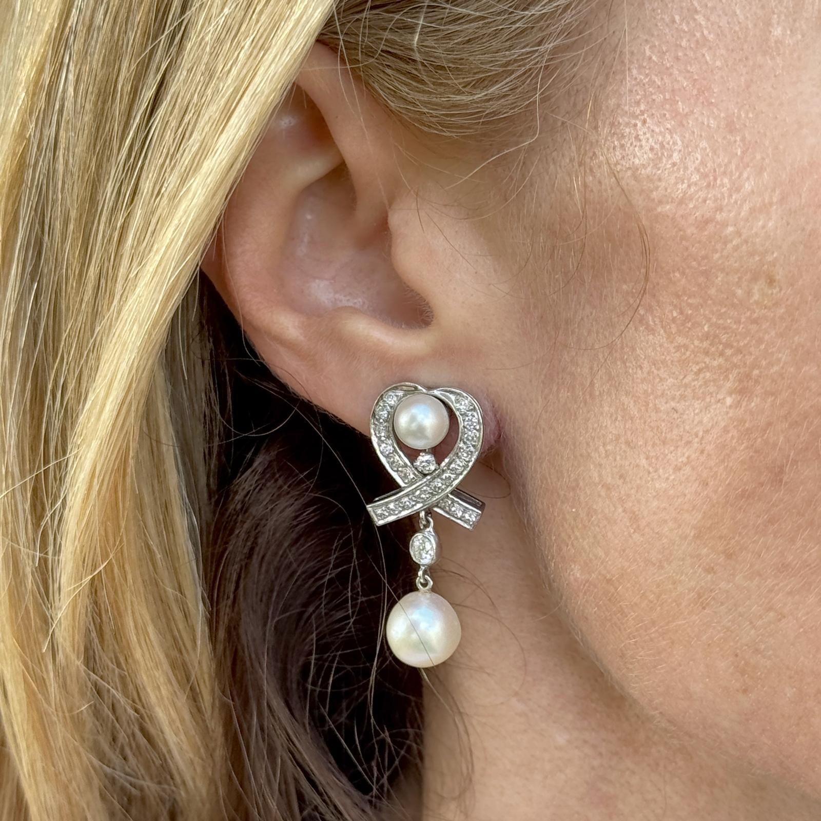 Vintage-Ohrringe aus 14 Karat Weißgold in Herzform mit Diamanten und Perlen, die zeitlose Romantik und raffinierte Handwerkskunst ausstrahlen. Jeder Ohrring zeichnet sich durch ein zartes Arrangement aus vier alten europäischen und runden Brillanten