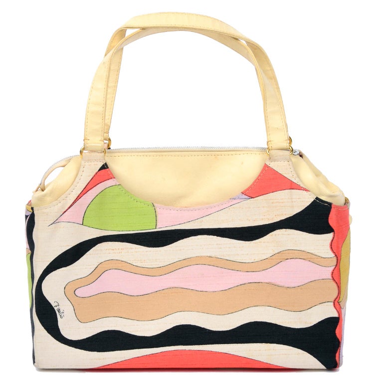 This is a vintage 1960's Emilio Pucci by Jana handbag in a signature Pucci printed raw silk and Cream / tan leather. This bag has top handles, gold tone metal hardware, and 2 gold metal feet. This vintage handbag closes with a metal zipper on the