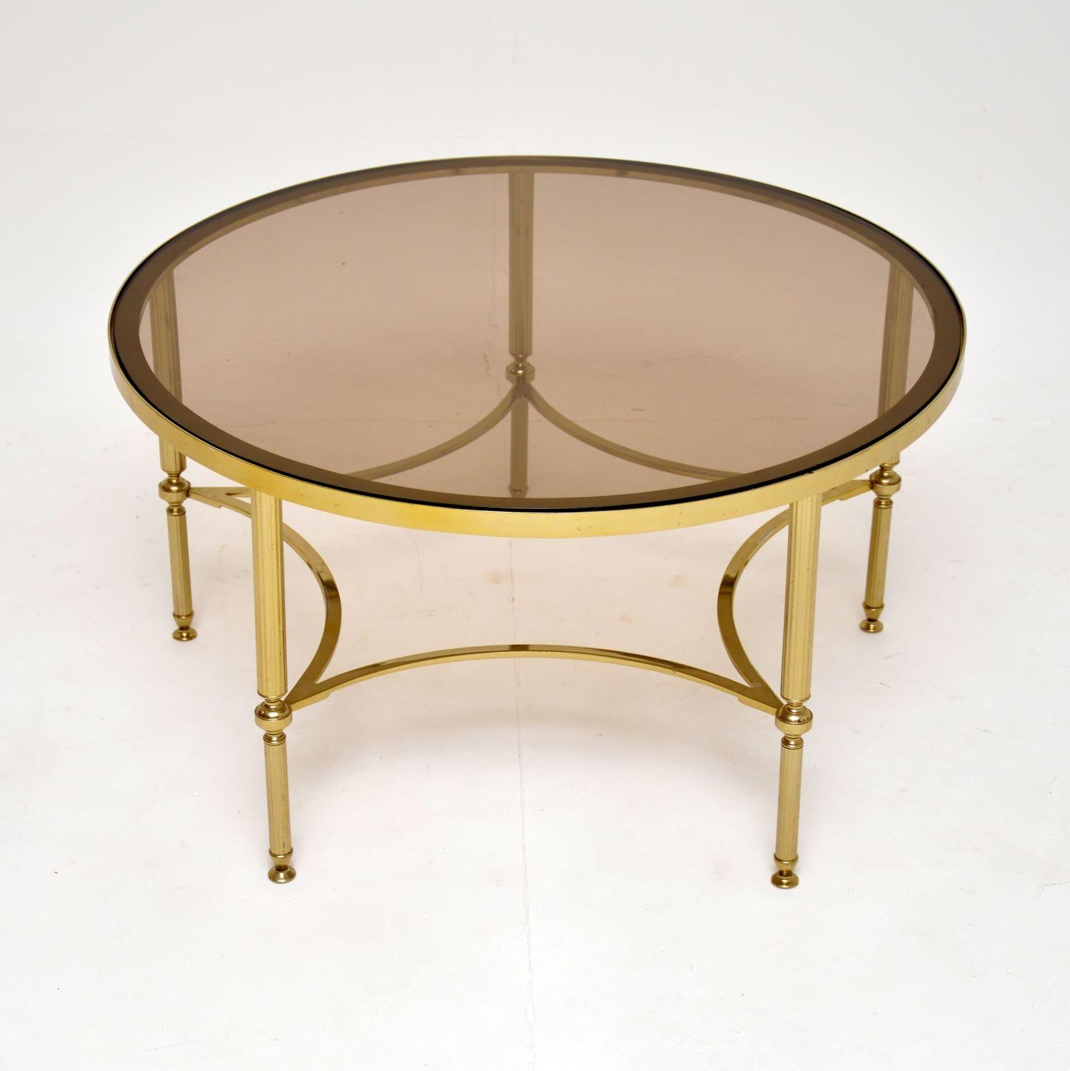 Une table basse en laiton et verre très élégante et extrêmement bien faite, datant des années 1960.

Il est d'une belle taille, le plateau circulaire a un verre encastré et repose sur cinq pieds cannelés reliés entre eux par des brancards.

L'état