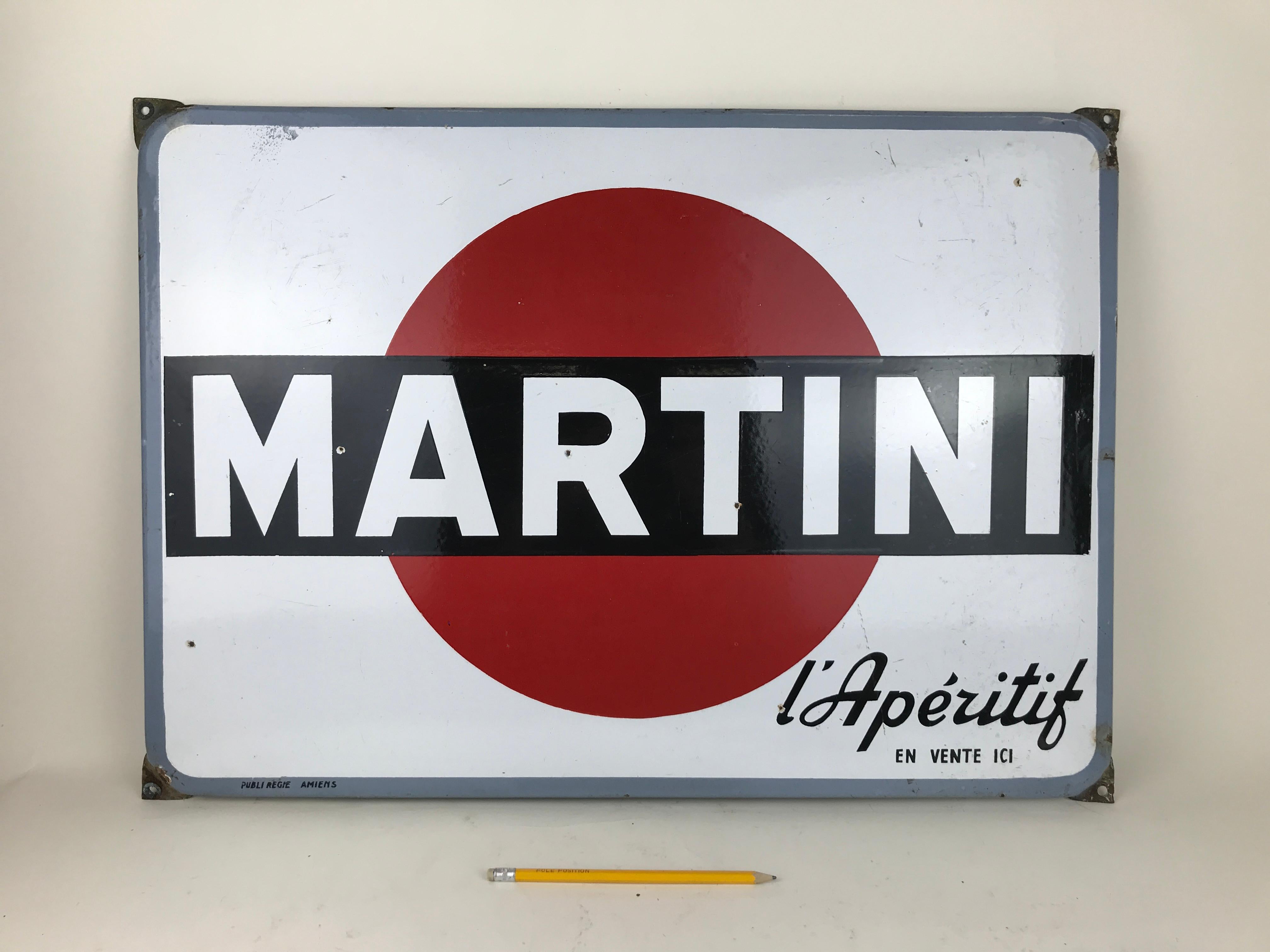 This enamel metal sign of Martini L' Aperitif was produced in the 1960s in France. 
In this advertising sign the Martini logo is placed on white background with advertising slogan 