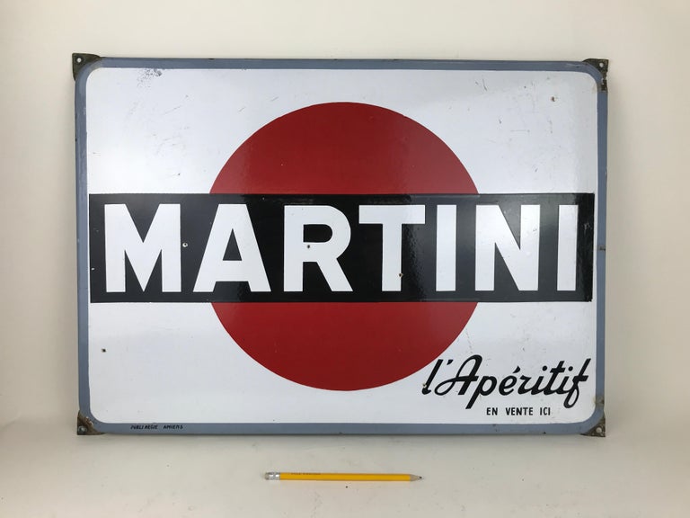 This enamel metal sign of Martini L' Aperitif was produced in the 1960s in France. 
In this advertising sign the Martini logo is placed on white background with advertising slogan 