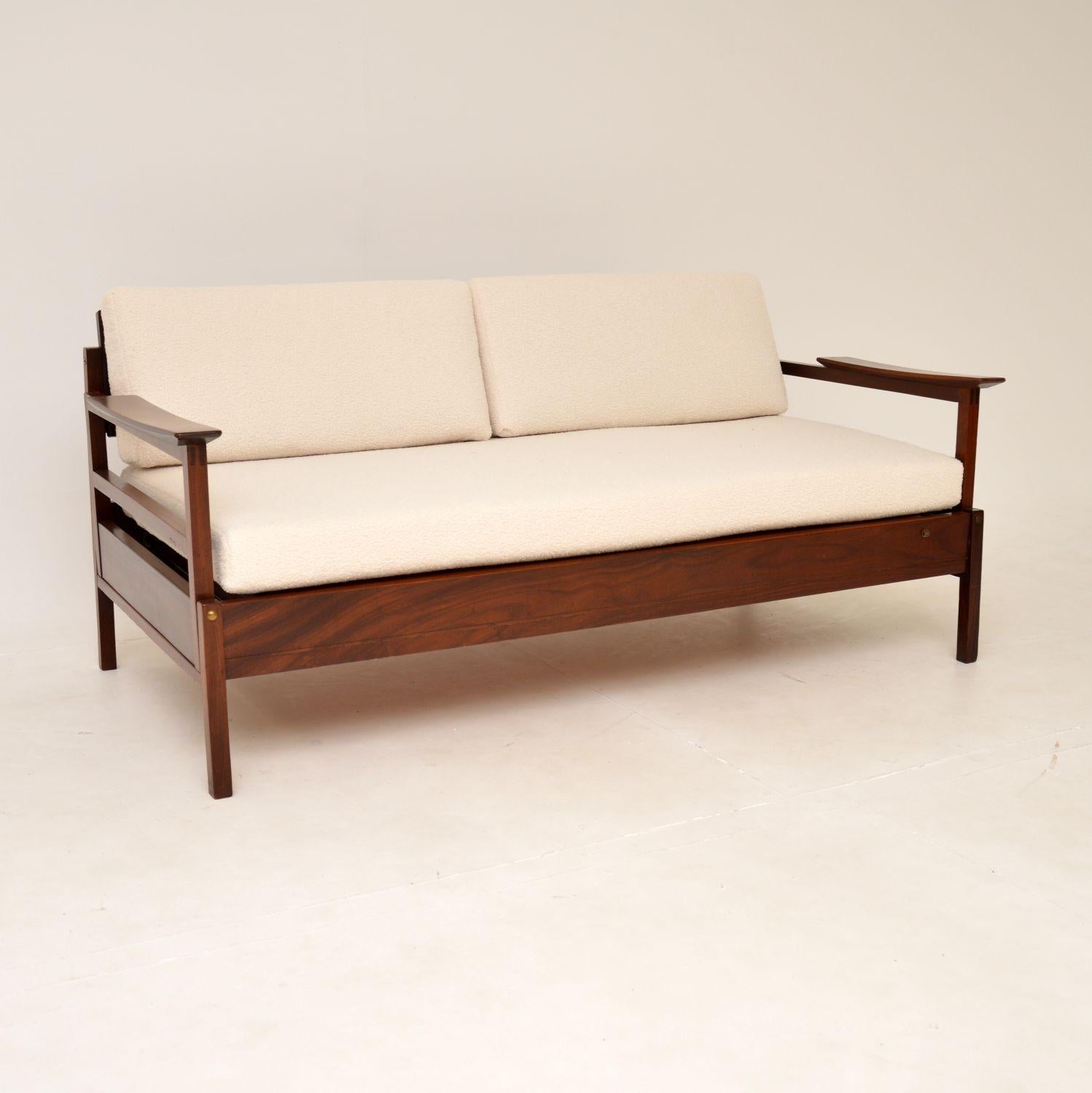 A stylish and very rare vintage ‘Gambit’ sofa bed by Guy Rogers. This was made in England during the 1960’s.

The frame is solid wood, which has gorgeous grain patterns and a beautiful, rich colour.

The arms drop down and the back cushions go
