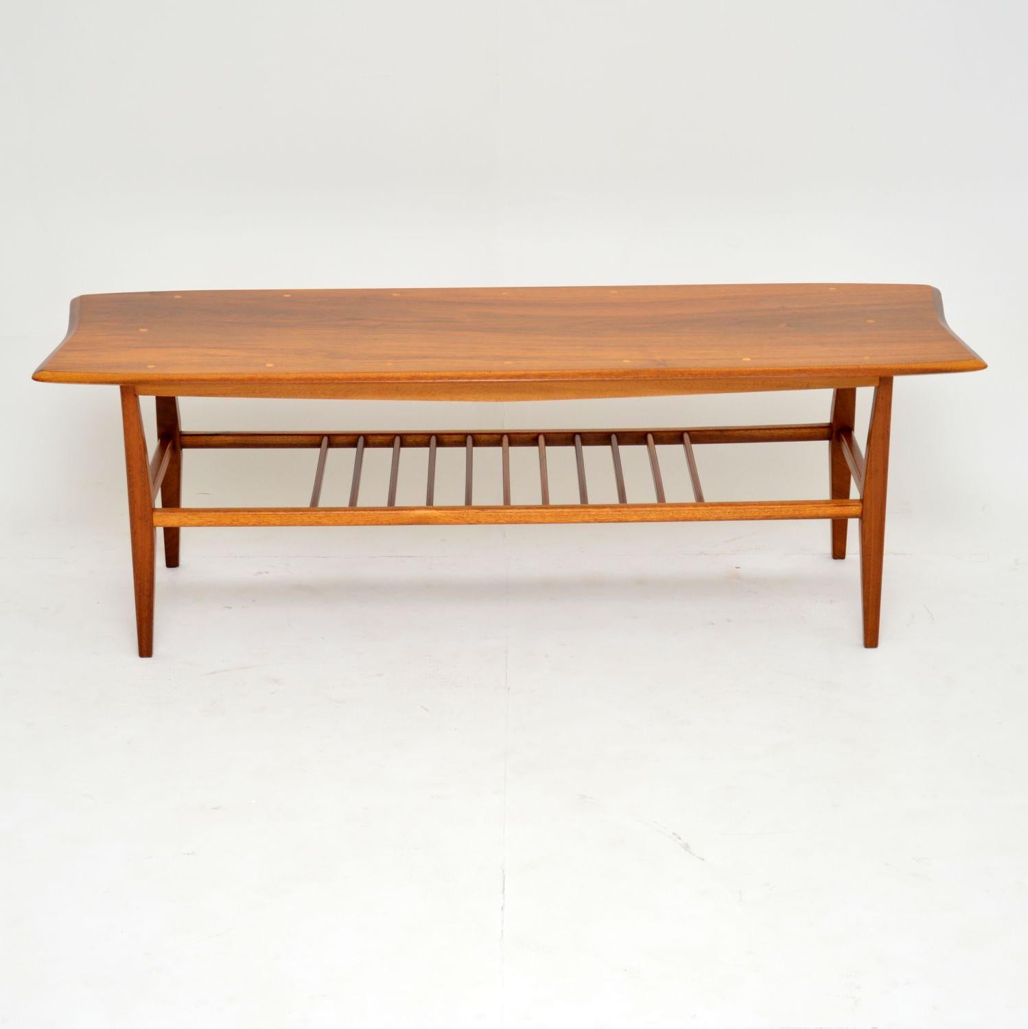 A beautifully styled and very well made coffee table in walnut. This dates from the 1960s, it was made in Britain. The walnut top has small inlaid circles of a lighter wood, possibly satin wood. This also has a useful lower tier. We have had this