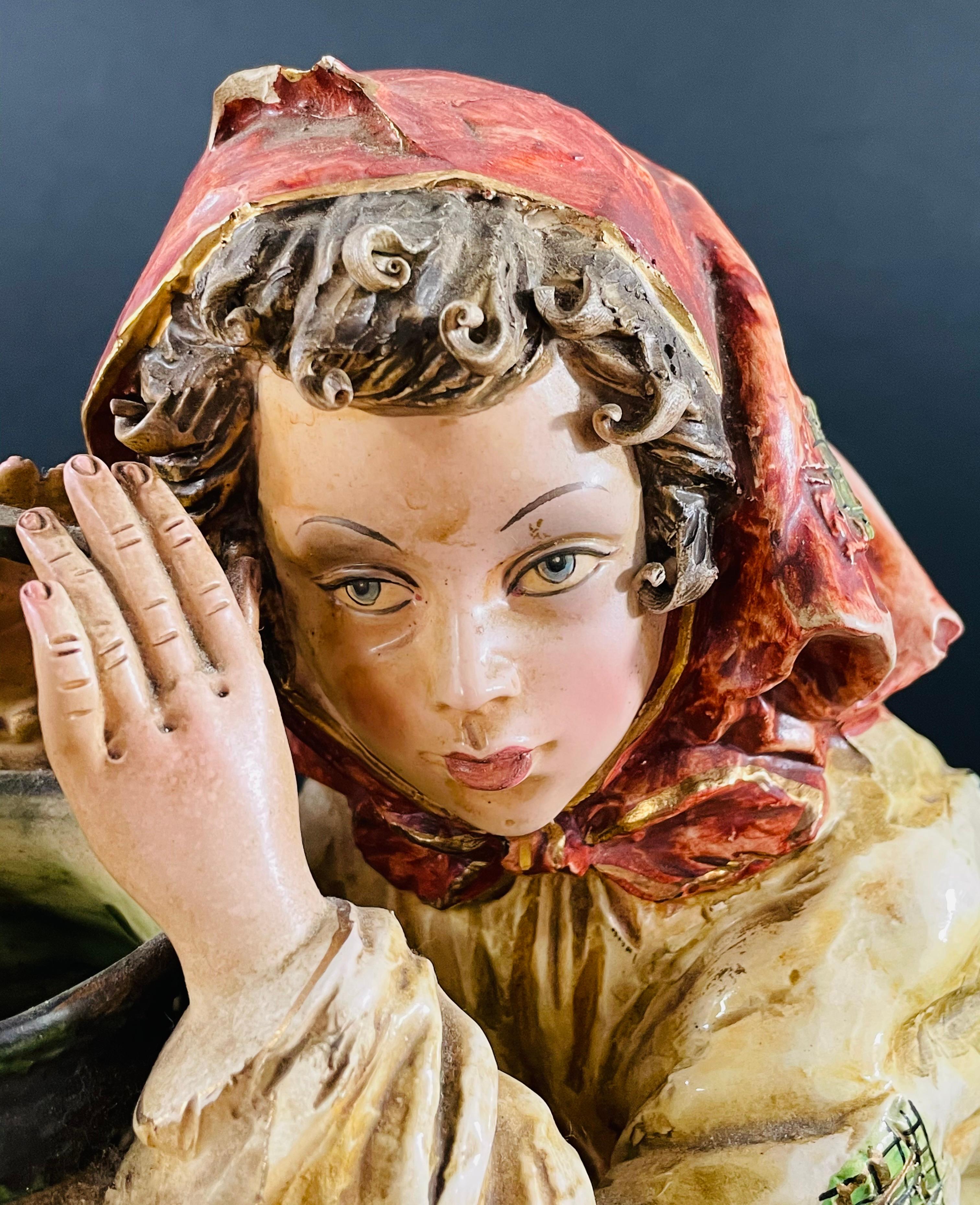 A 1970's vintage Italian porcelain sculpture or statue of a framer girl holding a jar. The statue features intricate details and is skillfully hand painted. The pensive farmer girl is setting on the floor while leaning on a small table and holding a