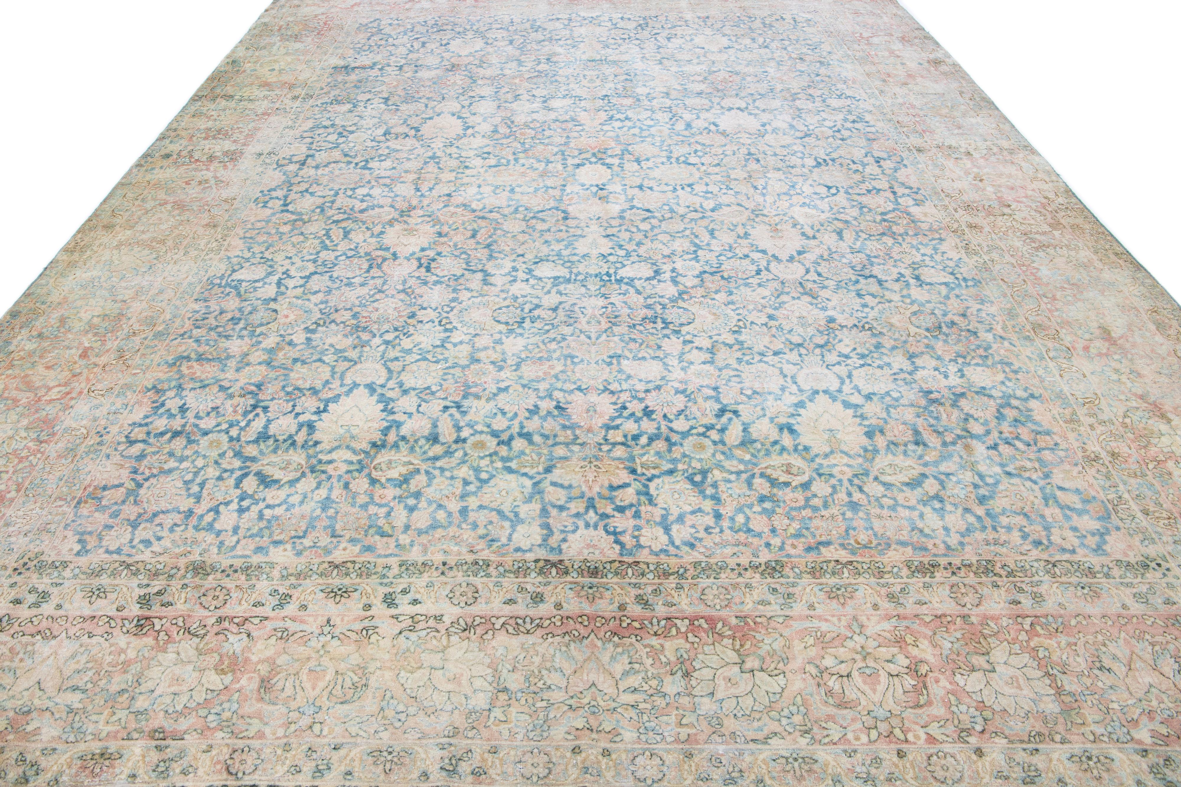 This piece is an exquisite, hand-knotted Kerman rug from vintage Persian craftsmanship. Its shabby chic woolen texture and navy blue main body give it a distinct allure. Embellished with a red-pink border, the rug sports a brown and blue that