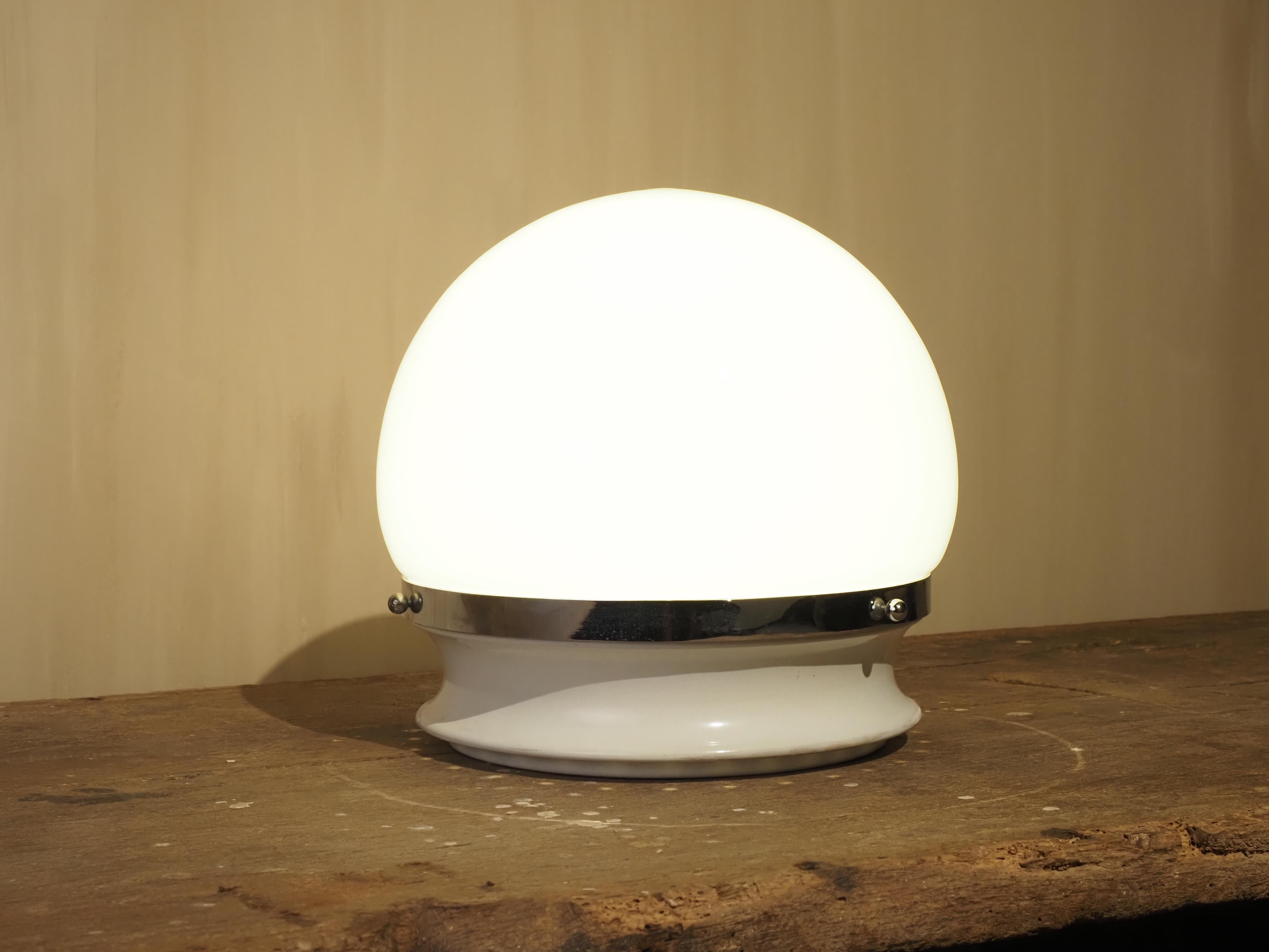 Esta elegante lámpara de sobremesa vintage presenta una llamativa pantalla redonda de cristal opalino, bellamente contrastada con un aro cromado de acento. Su diseño atemporal de mediados de siglo crea un resplandor cálido y atmosférico, que lo