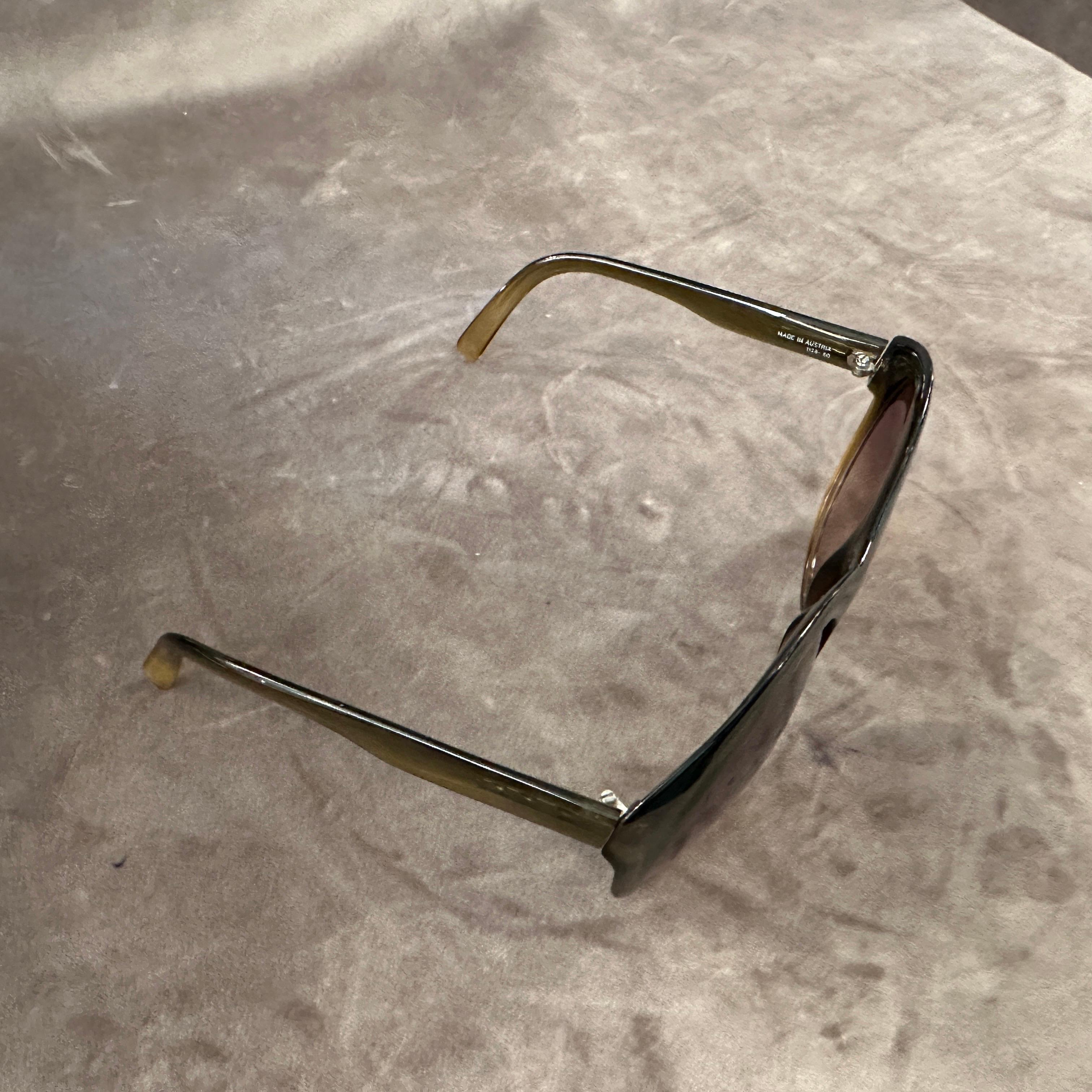 Ce site  est une paire de lunettes de soleil vintage de Viennaline. Elles présentent une forme arrondie et surdimensionnée avec une monture épaisse en acétate vert olive. Un Label sur la lentille identifie la marque comme Viennaline et indique que