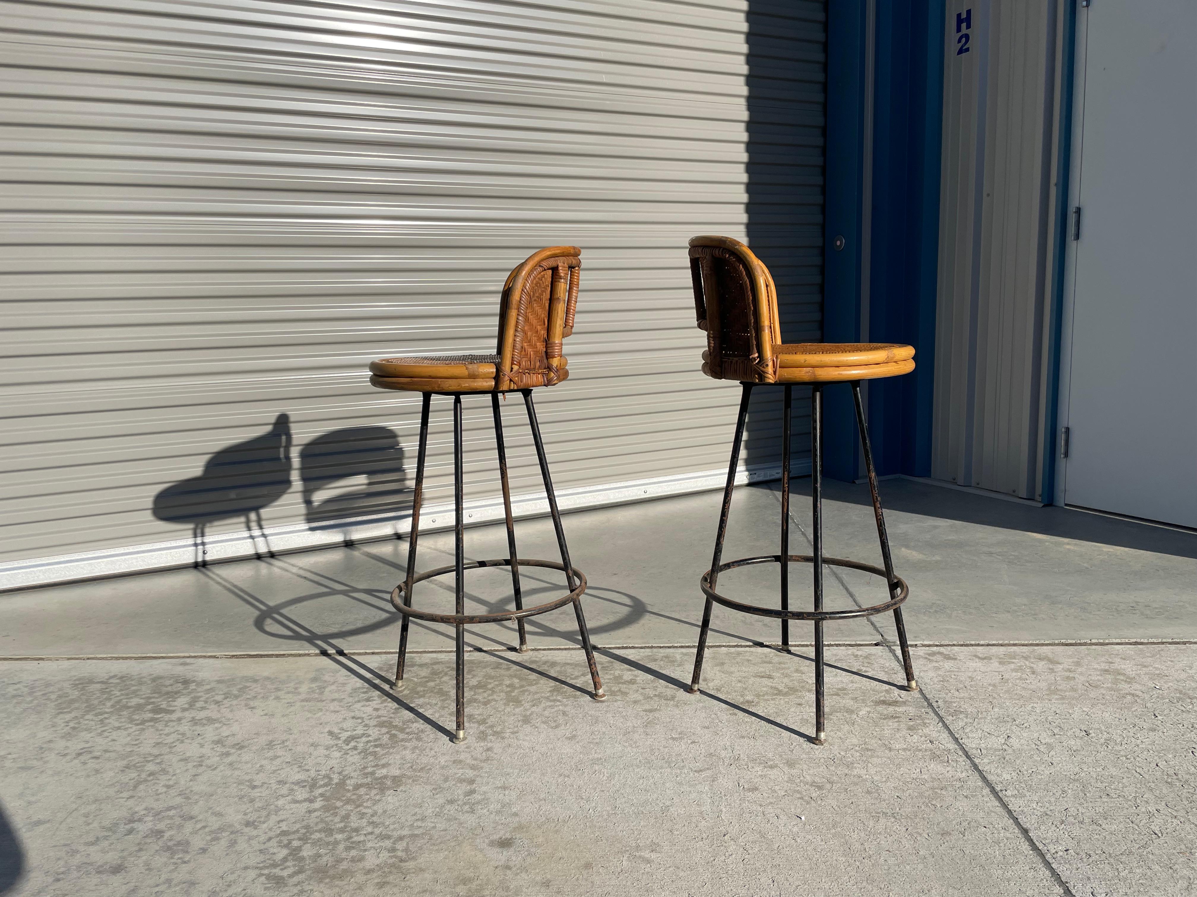 Vintage pair of whicker swivel counter stools designed and manufactured in the united states, circa 1960s. This beautiful pair of stools were styled after Danny Ho Fang. They feature a whicker frame design with a black-finished metal base.