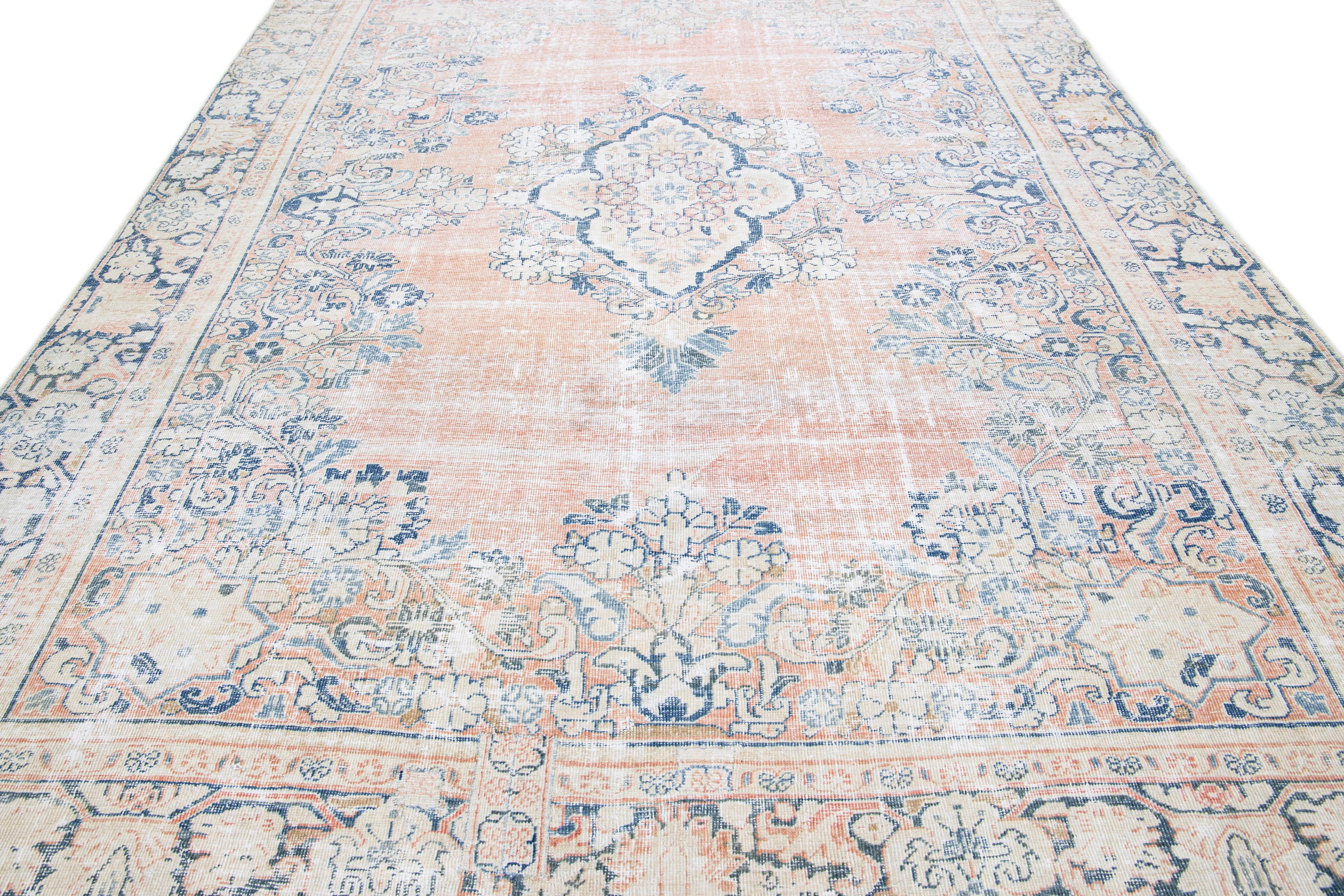 The hand-knotted wool and captivating medallion design Heriz rug exude elegance. The intricate floral pattern, beautifully constructed with detailed geometric shapes and vibrant blue accents, enhances the soft peach field, elevating it into a