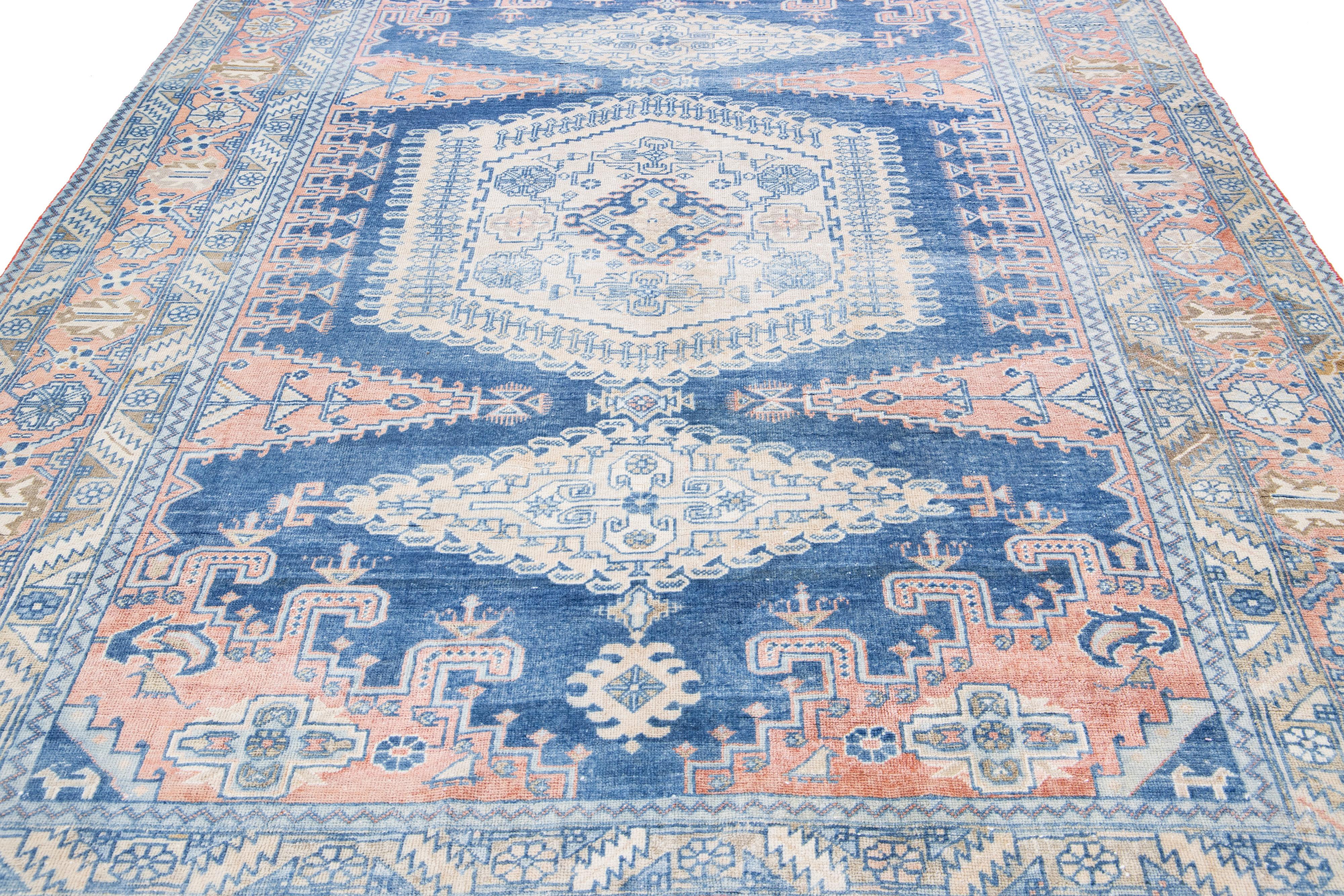 The hand-knotted wool and captivating medallion design Heriz rug exude elegance. The intricate floral pattern, beautifully constructed with detailed geometric shapes and vibrant blue accents, enhances the soft peach field, elevating it into a