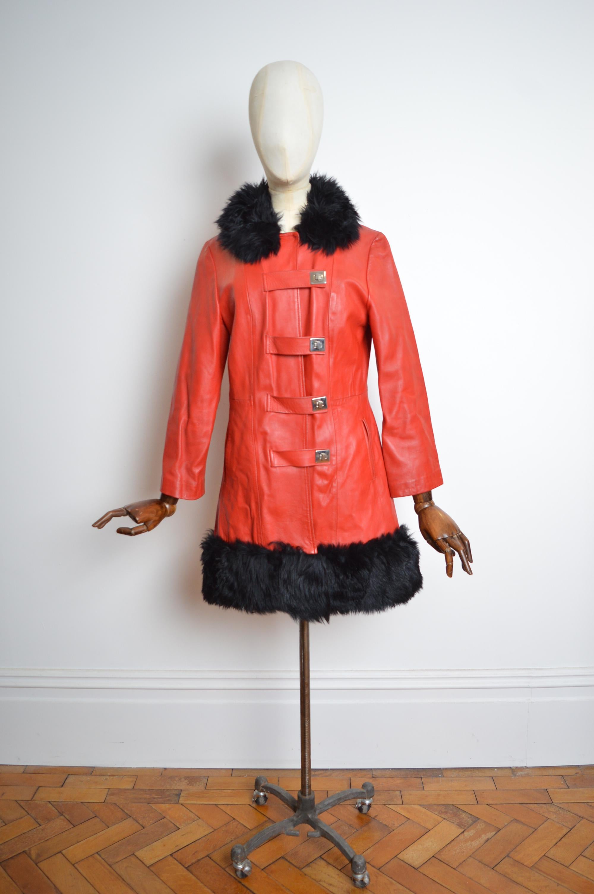 Hervorragender Vintage Ledermantel im Penny Lane's Stil um 1960, in kirschrot mit kontrastierendem schwarzem flauschigem Shearling-Kragen und Saum. Chrombeschläge mit Drehverschlüssen. 
Grube zu Grube; 19