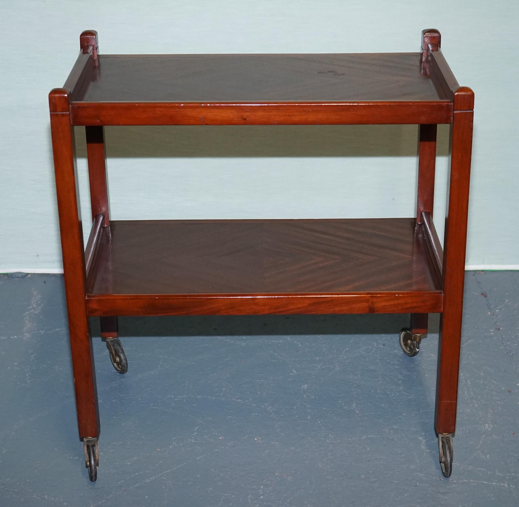 
Antiques of London



This charming vintage two-tier tea trolley combines elegant simplicity with mid-century functionality. Crafted in warm-toned wood with a smooth, polished finish, it features two spacious rectangular trays with raised edges to