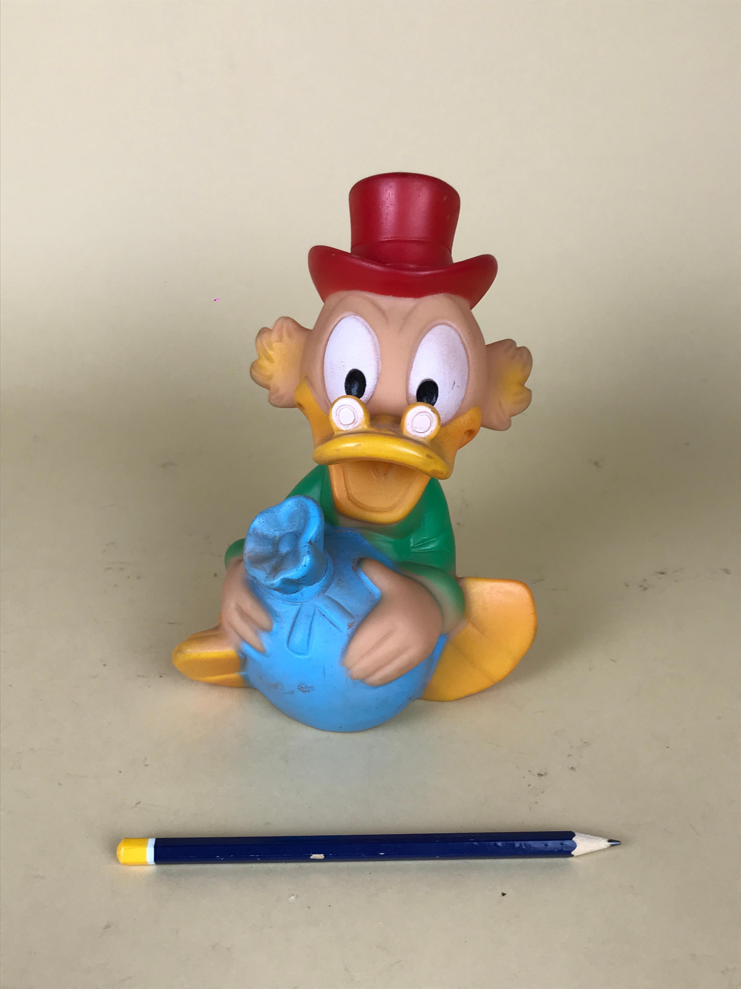 Vintage green, red and blue Uncle Scrooge squeak rubber toy with hat and a bag of coins made by Jugasa in Spain the 1960s for Disney.

Marked 