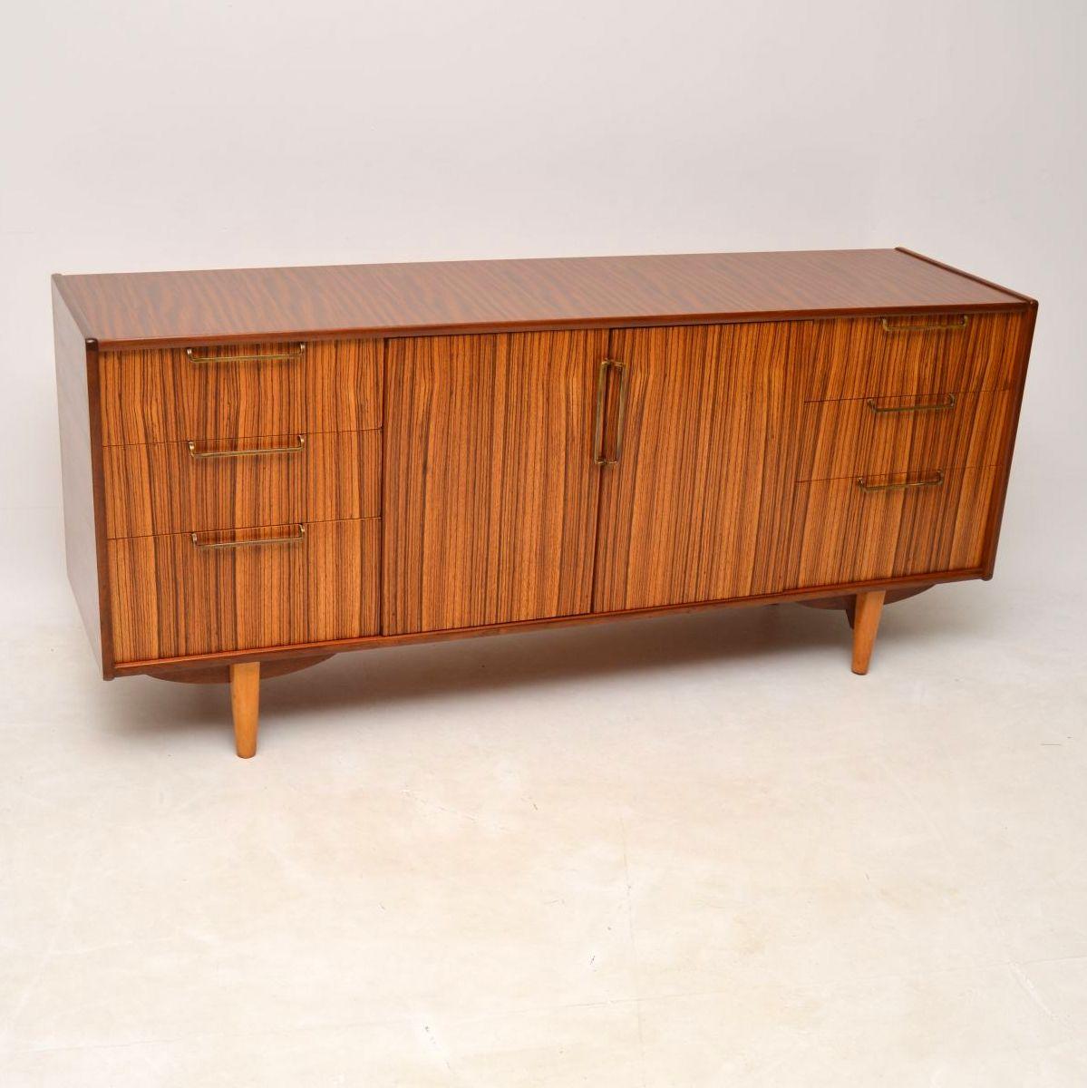 A stylish and unusual design, this vintage sideboard was made by Elliots of Newbury, it dates from the 1960s. The drawer and door fronts are made from beautifully grained zebrano, with brass handles, the top and sides are walnut. We have had this