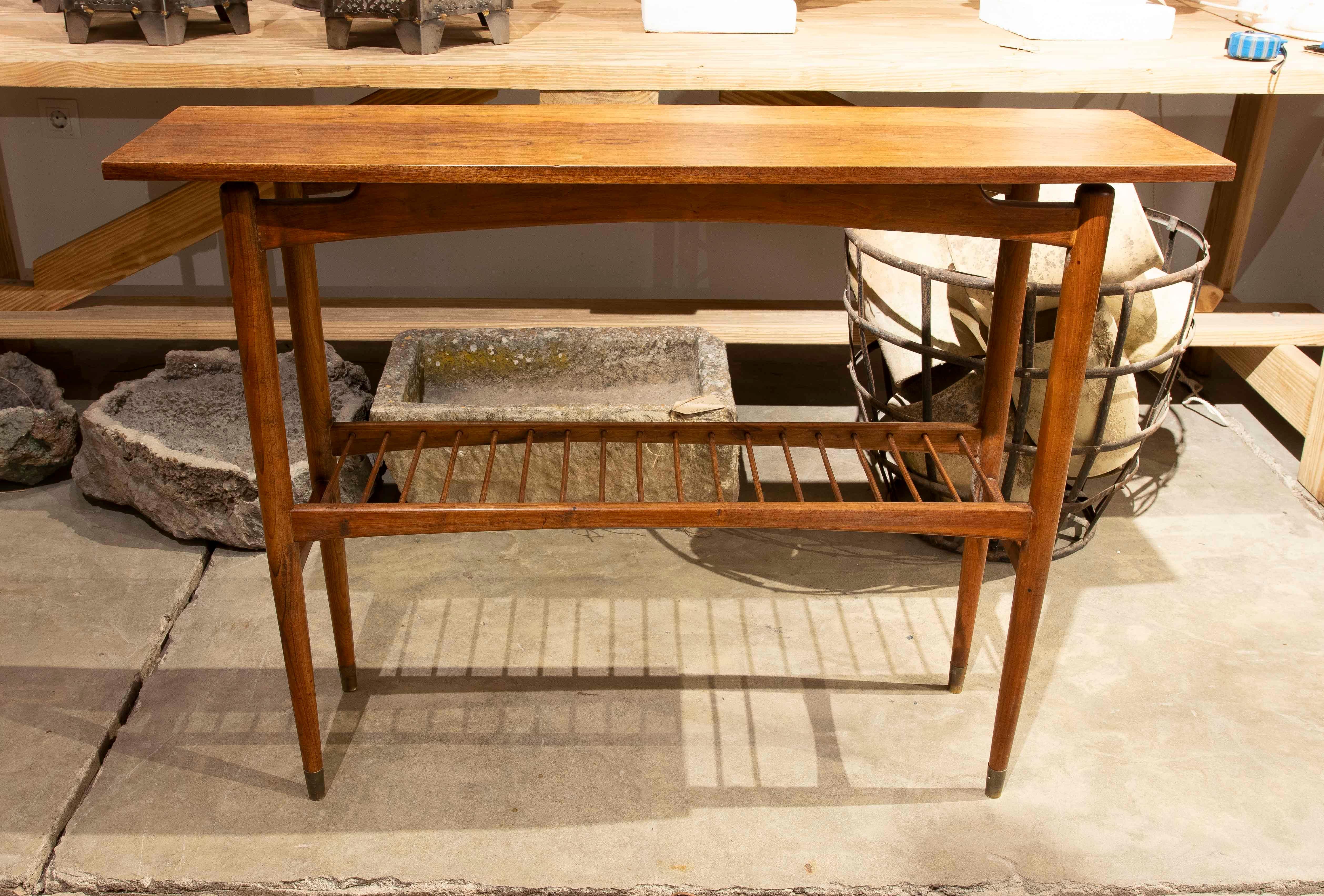 A light and functional console table made of solid wood, ideal for hallways or entryways. Its elongated, simple top is complemented by a lower shelf with bars that provides additional storage or decorative space. The style is reminiscent of