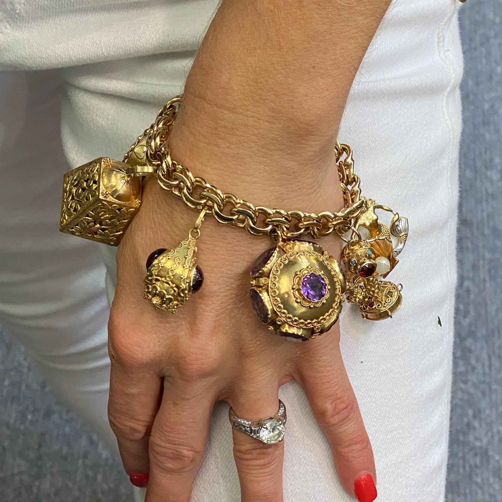 Fabulous charm bracelet fashioned in 14 and 18 karat yellow gold. The bracelet features 8 large vintage charms featuring amethyst and garnet gemstones, seed pearls, and turquoise. The bracelel, which measures 7.5 inches in length, is 14 karat yellow