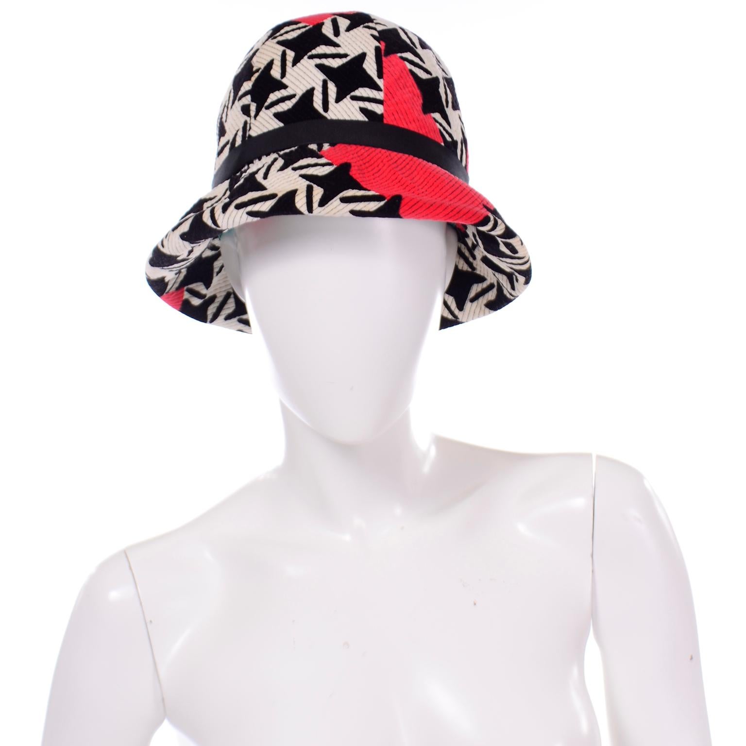 This is a rare vintage 1960's Yves Saint Laurent bucket hat in a bold, graphic print. The hat is made of velvet in a black and white modified houndstooth or pinwheel pattern print with red geometric abstract shapes and black top stitching. There is