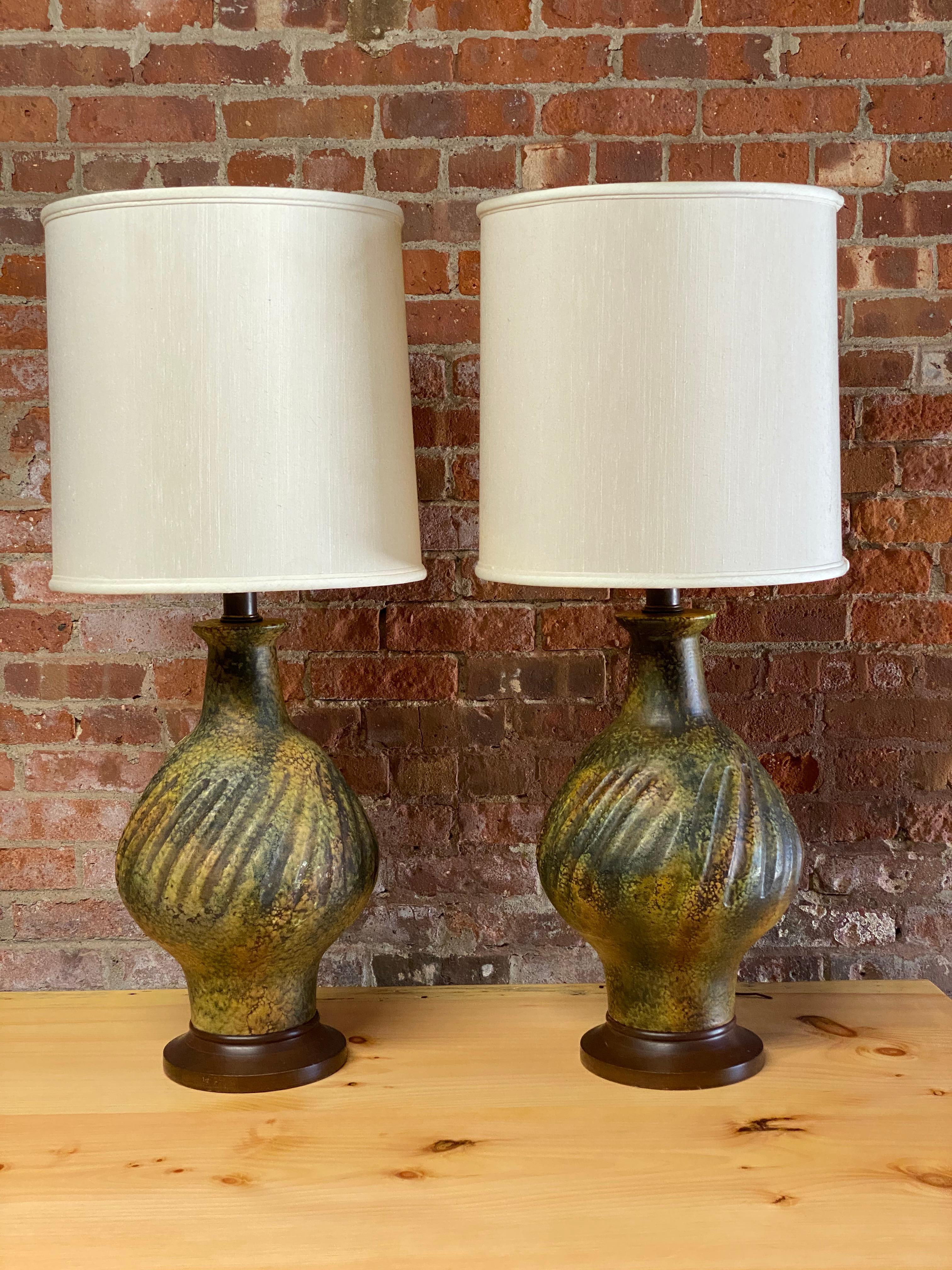 A pair of volcanic ceramic table lamps done in a mottled green/yellow glaze. Cast ceramic bodies with solid wood bases, Circa 1960-70. Very good condition with original wiring.

Shades are for photography purposes only and not included. Harps