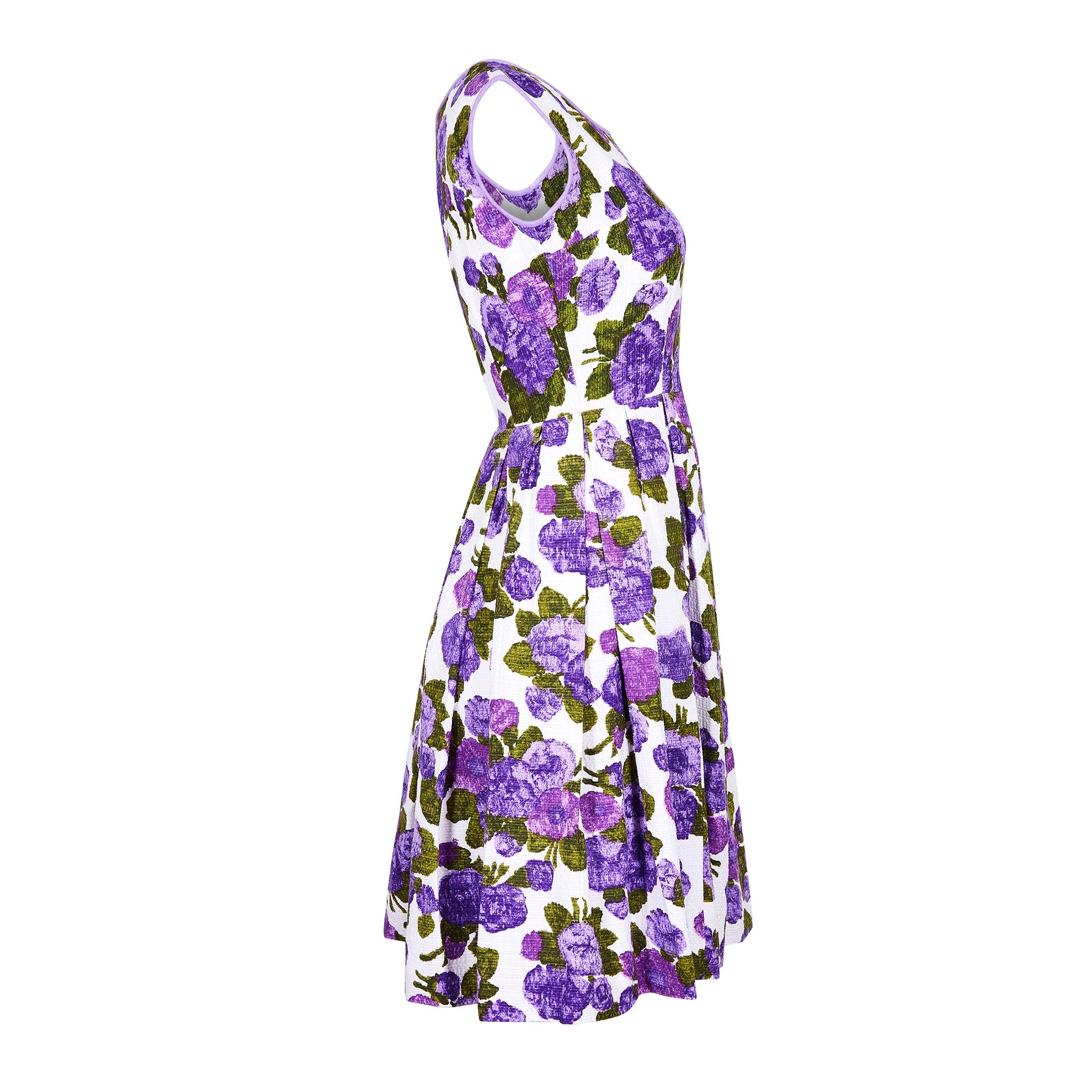 This dress is a particularly vibrant and fresh example of late 1950s or early 1960s summer fashion. It is comprised of an unusual textured cotton fabric with a bold purple and green floral repeat pattern. The label represents this style as Italian