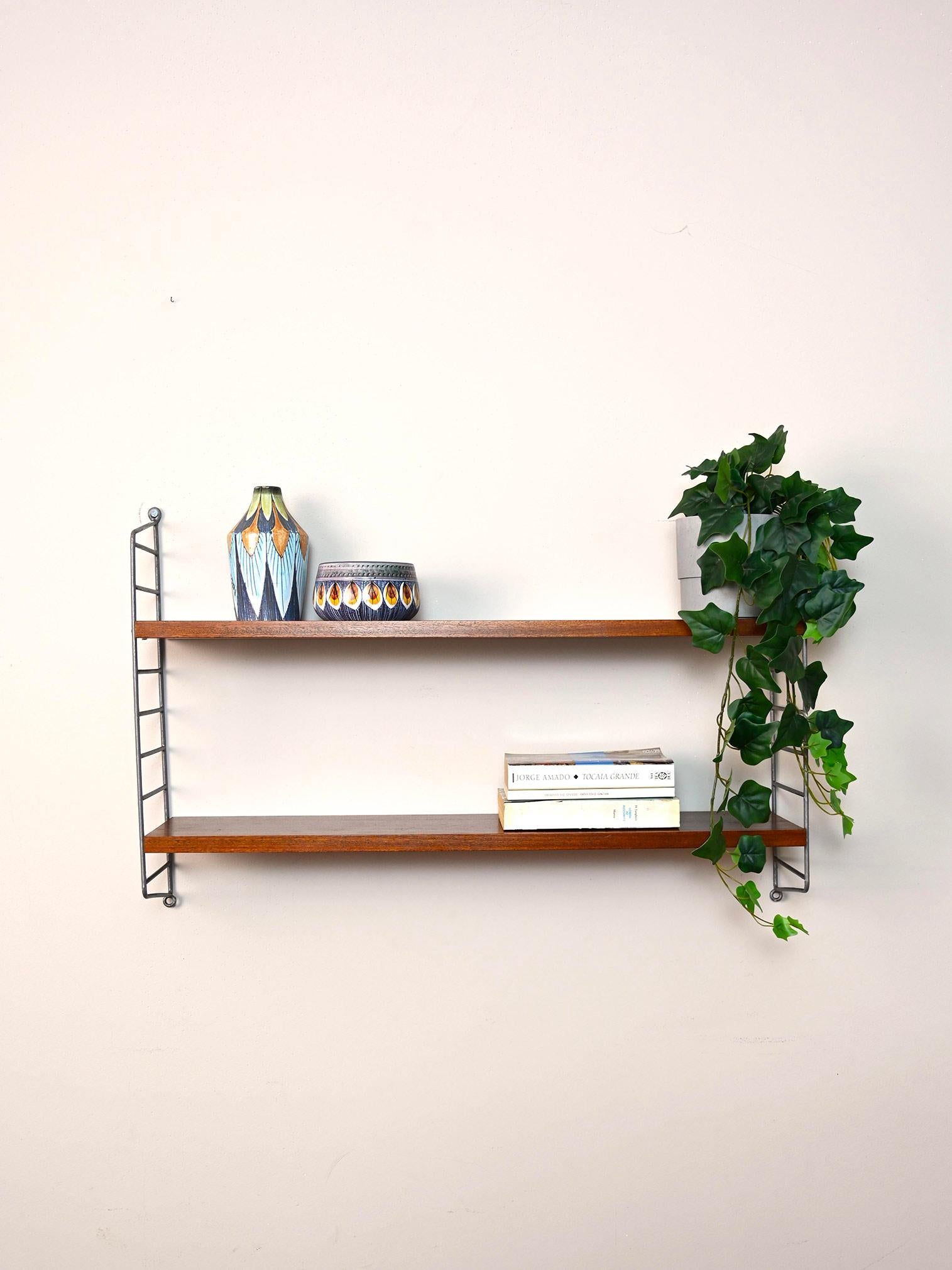 Original Scandinavian shelves from the 1960s.

This simple shelving system consists of a black metal side frame on which two wooden shelves rest.
Simple and functional it can be hung in different rooms of the house.

Good condition. It has been