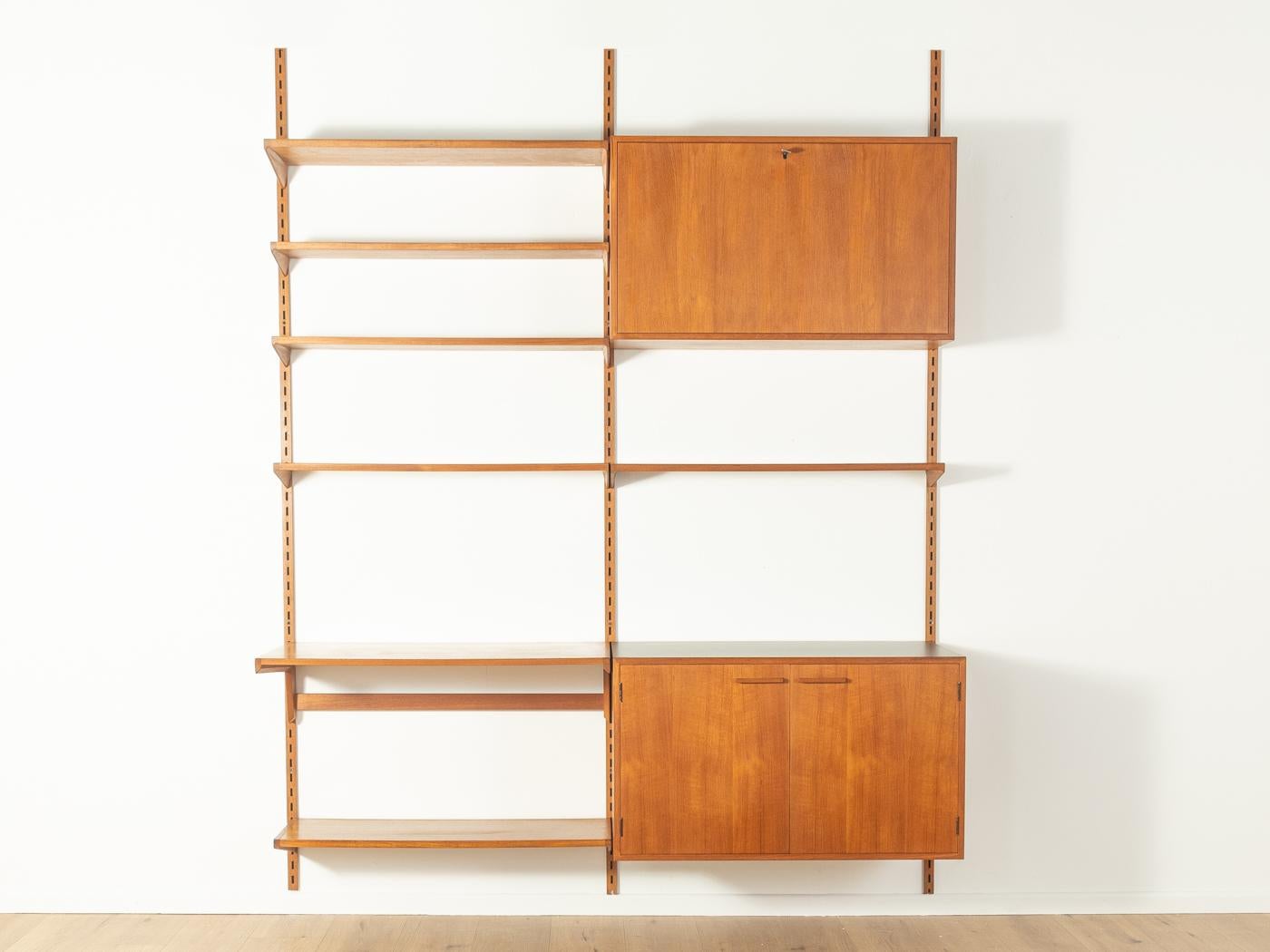 Classic shelving system from the 1960s. The high-quality containers and shelves are veneered in teak. The system consists of six shelves, a writing surface, one container with two doors Formica-coated surface in black and two shelves, one container