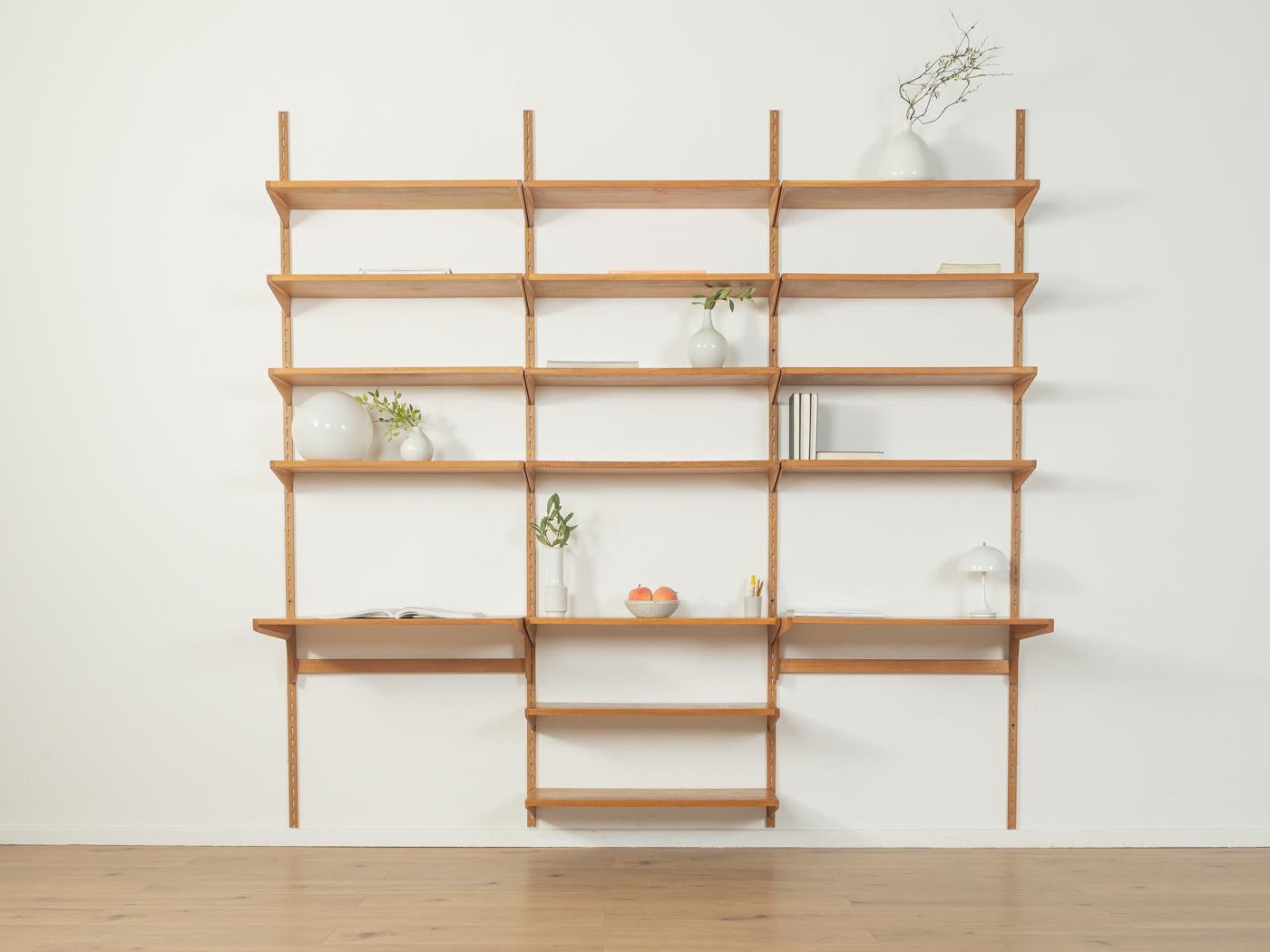 Classic wall shelf from the 1960s. The high-quality shelves are veneered in oak. The system consists of 17 shelves and four ladders made of aluminum and oak veneer.

Quality Features:
accomplished design: perfect proportions and visible attention to