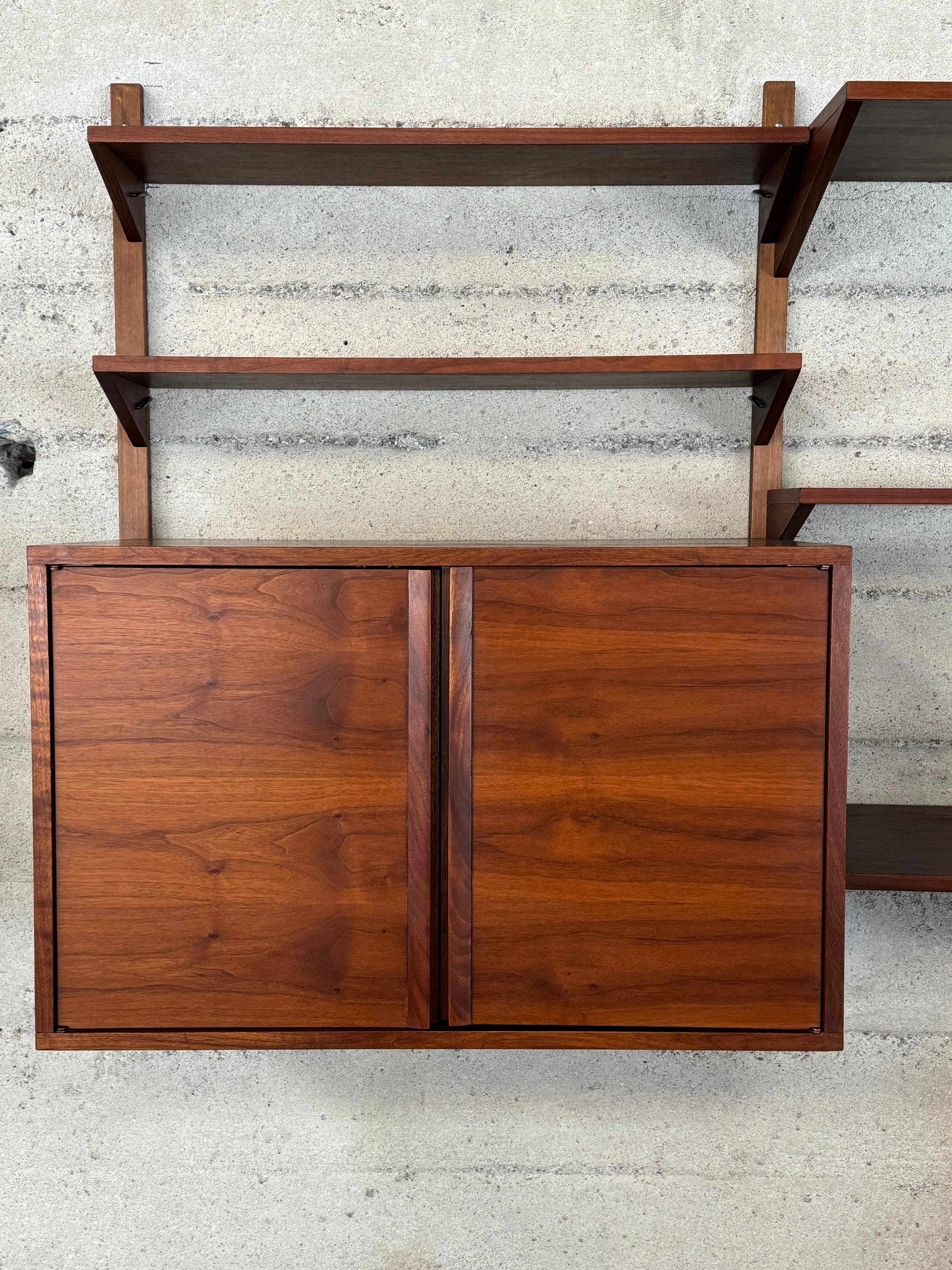 1960s wall unit with two storage cabinets with an adjustable shelf, five adjustable shelves and the sixth that can be used as a desk with a cutout for a power cord. Richly colored and grained walnut, the shelves and cabinets attach via u shaped