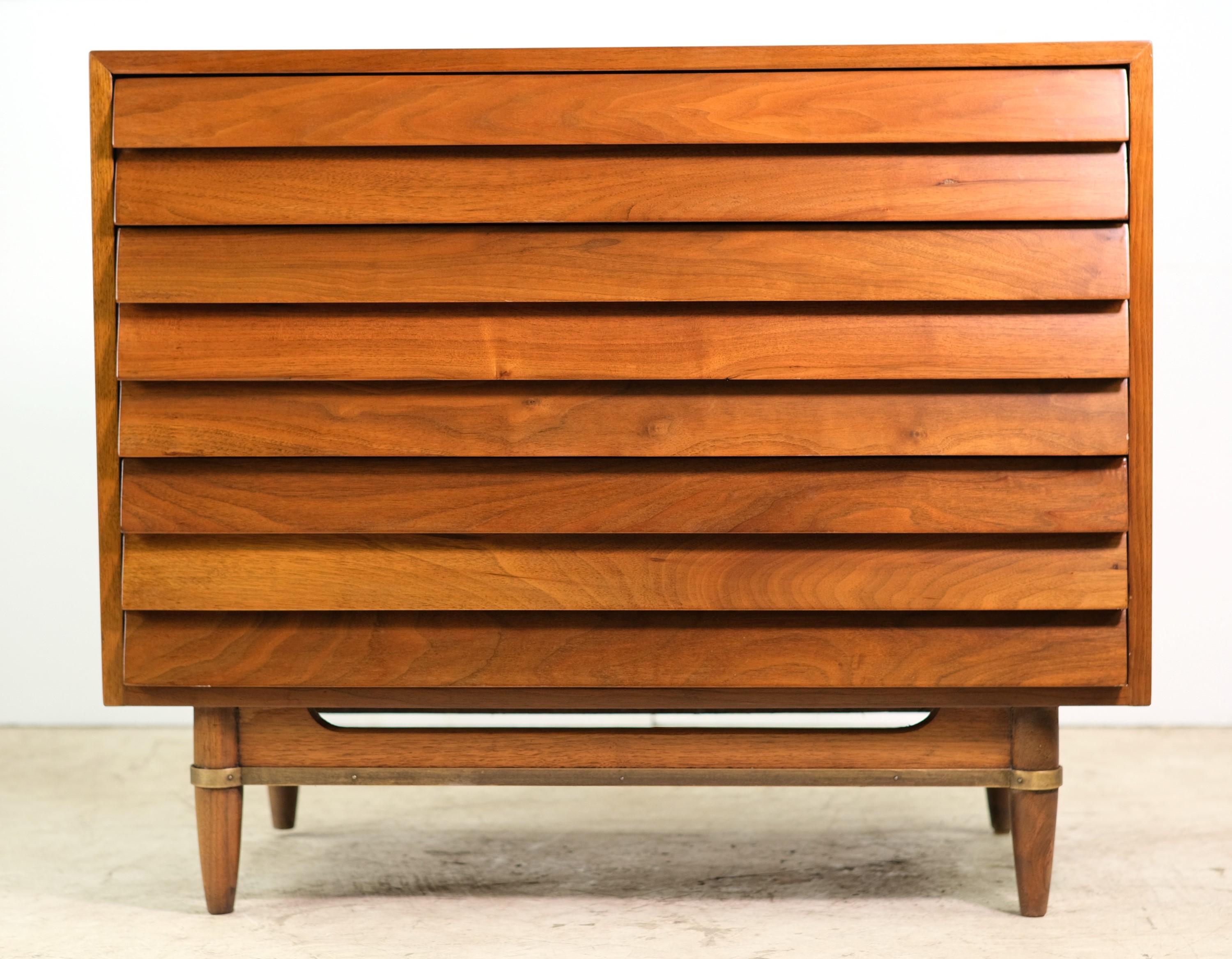 Mid-Century Modern three drawer credenza made of solid walnut with louvered front doors. It has dovetailed drawers with an oak interior and turned legs with a brass detailed base. Made by American Martinsville. It is well preserved for its age. This