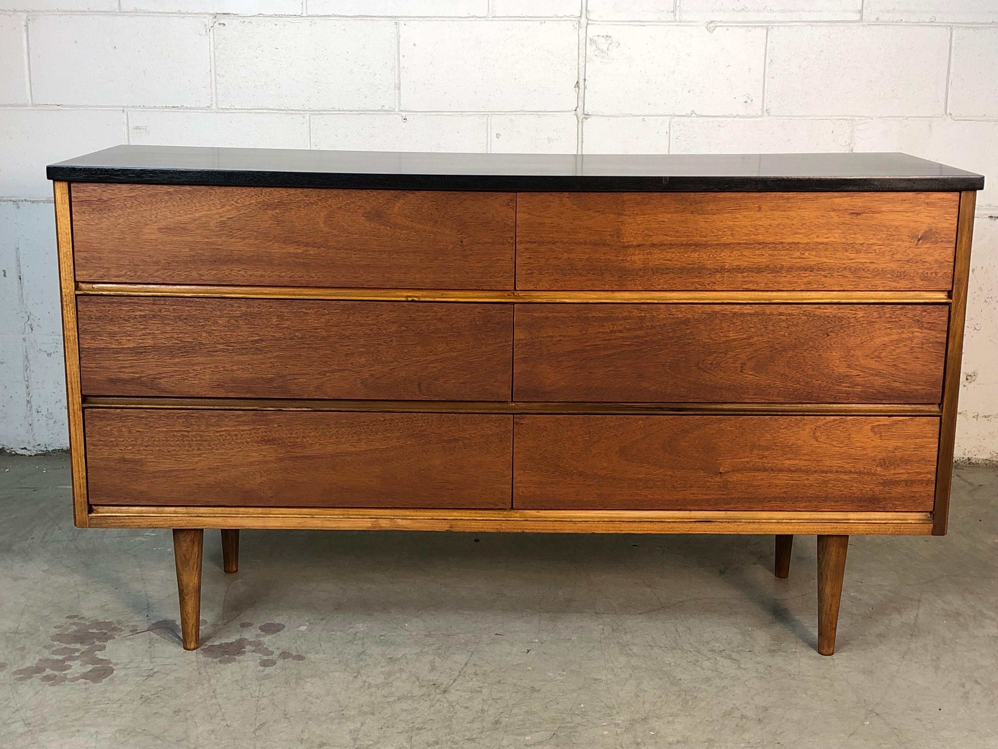 Vintage Mid-Century Modern 1960s walnut six drawer low dresser with a black painted top. The dresser has been recently refinished. There is some lighter ashwood that accents the dresser. The pulls are flush under the drawers and the legs are round.