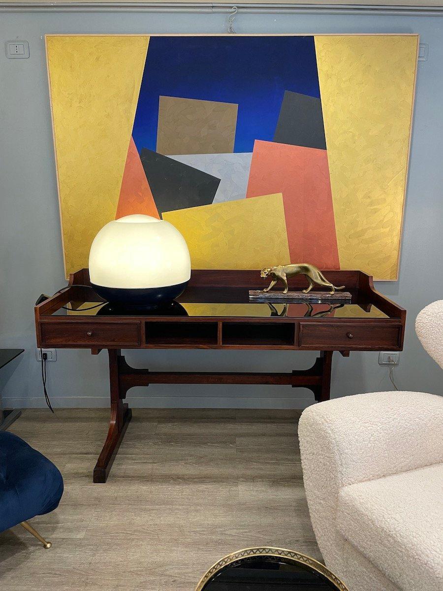 Scrivania in noce del 1960 con due cassetti e un vano centrale aperto. La struttura poggia su due gambe di sostegno ed è finemente rifinita su entrambi i lati, permettendo di posizionarla al centro di una stanza.

Misure: L 149 × P 61,5 × H 85