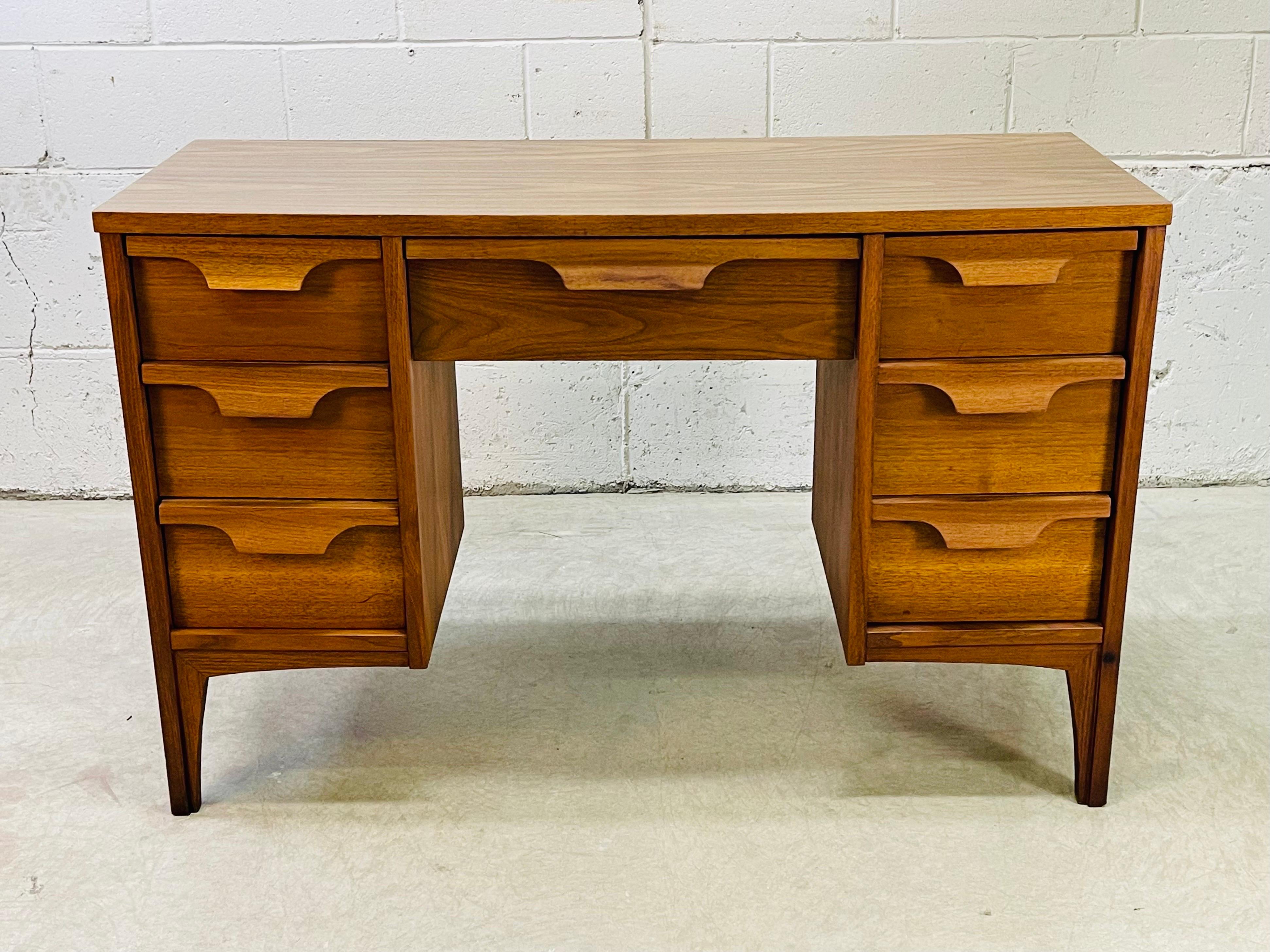 Vintage 1960s walnut wood and laminate top writing desk with seven drawers. The desk drawers have solid walnut sculpted pulls. Knee clearance is 20”W x 23”H. Marked 1960 on the back.