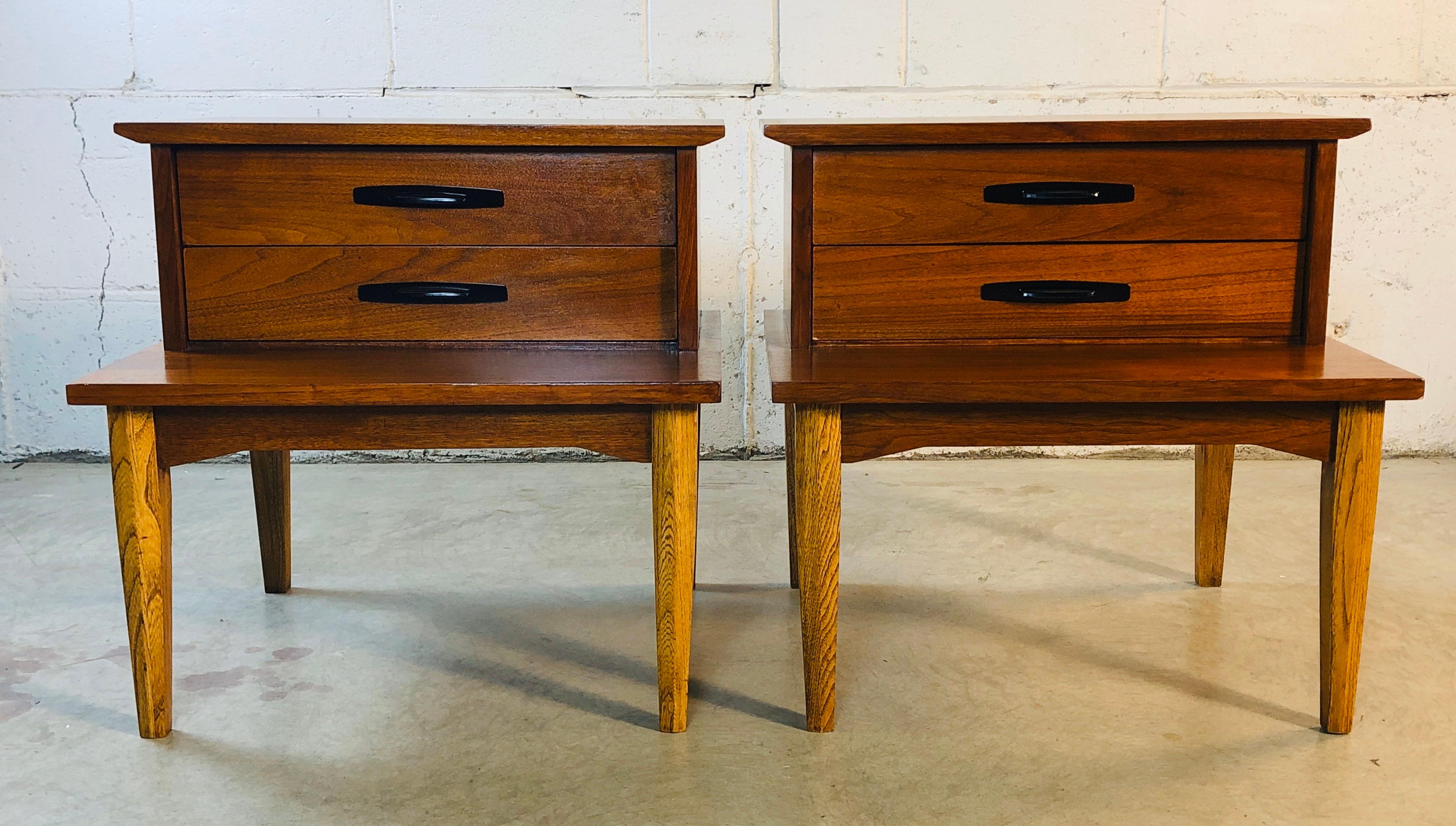 1960s walnut wood step-back style pair of bedroom nightstands by Dixie Furniture Co. The nightstands each have two drawers for storage. They are in restored and refinished condition. Marked in drawer.