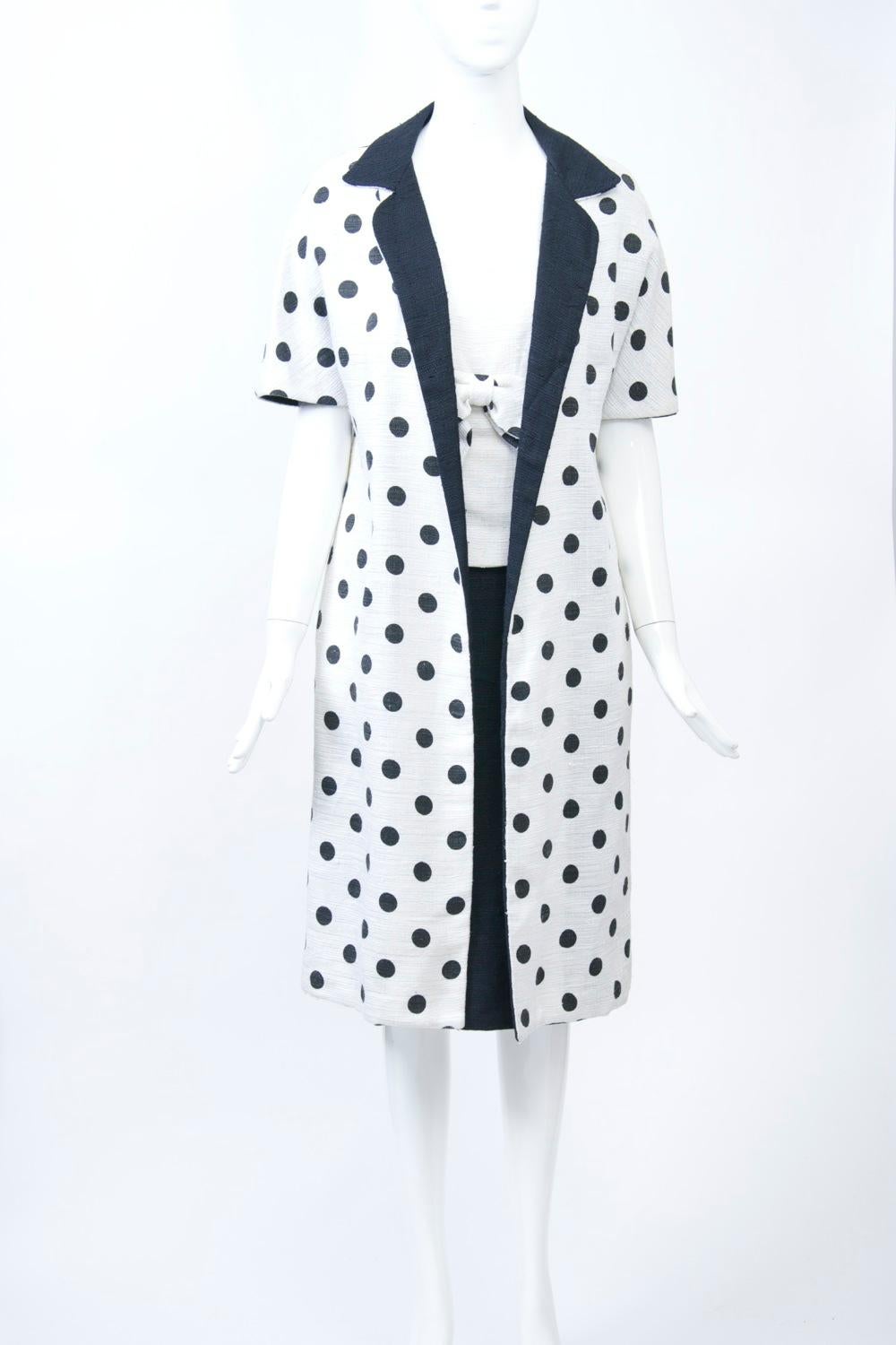 1960s summer weight dress and coat ensemble in linen-blend fabric, the short-sleeve, open coat in white with black polka dots throughout; its black lining provides the collar and facing. Underneath is a one-piece sleeveless dress that's styled as a
