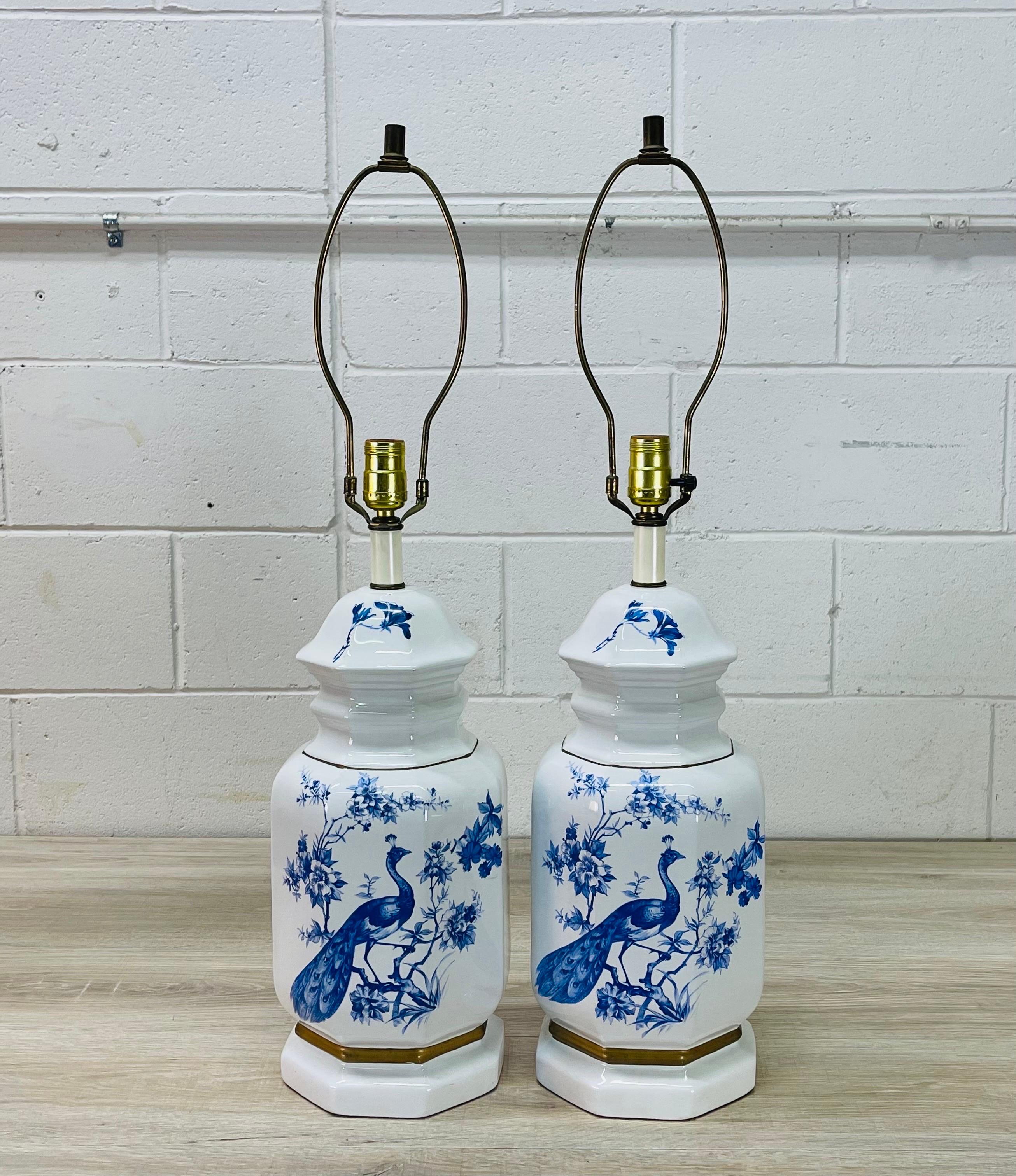 1960s Pair of white and blue peacock ceramic table lamps with a gold accented band. Back of the lamps have a floral design. Wired for the US and in working condition. Socket, measures: 21” height Harp, 5” diameter x 9.5”height. Uses a standard 100W