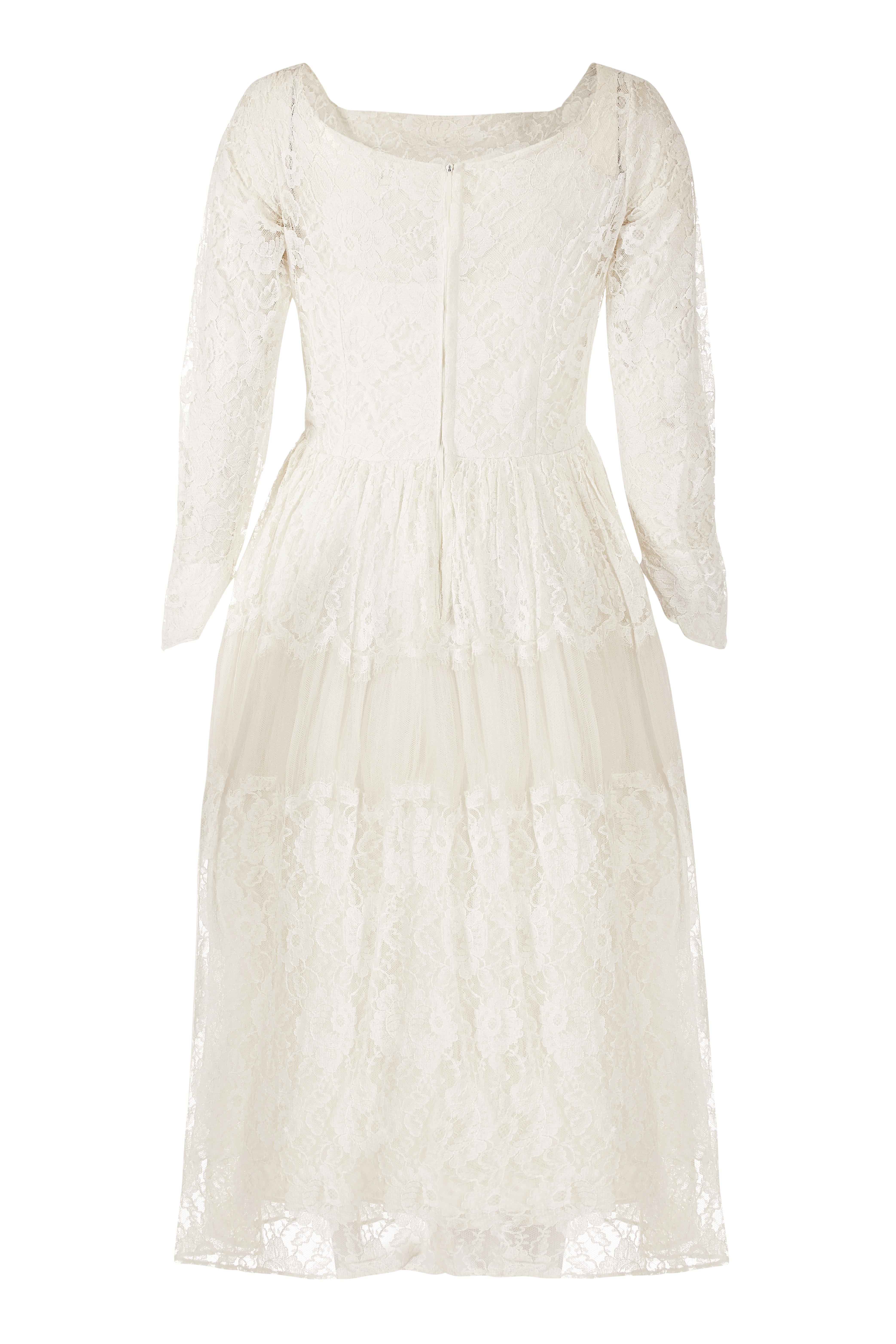 This pretty early 1960s or late 1950s white Chantilly style lace bridal gown has a fairy tale charm. The man-made, Chantilly style lace overlay covers the dress in its entirety and features a delicate floral design. The lace on the skirt is