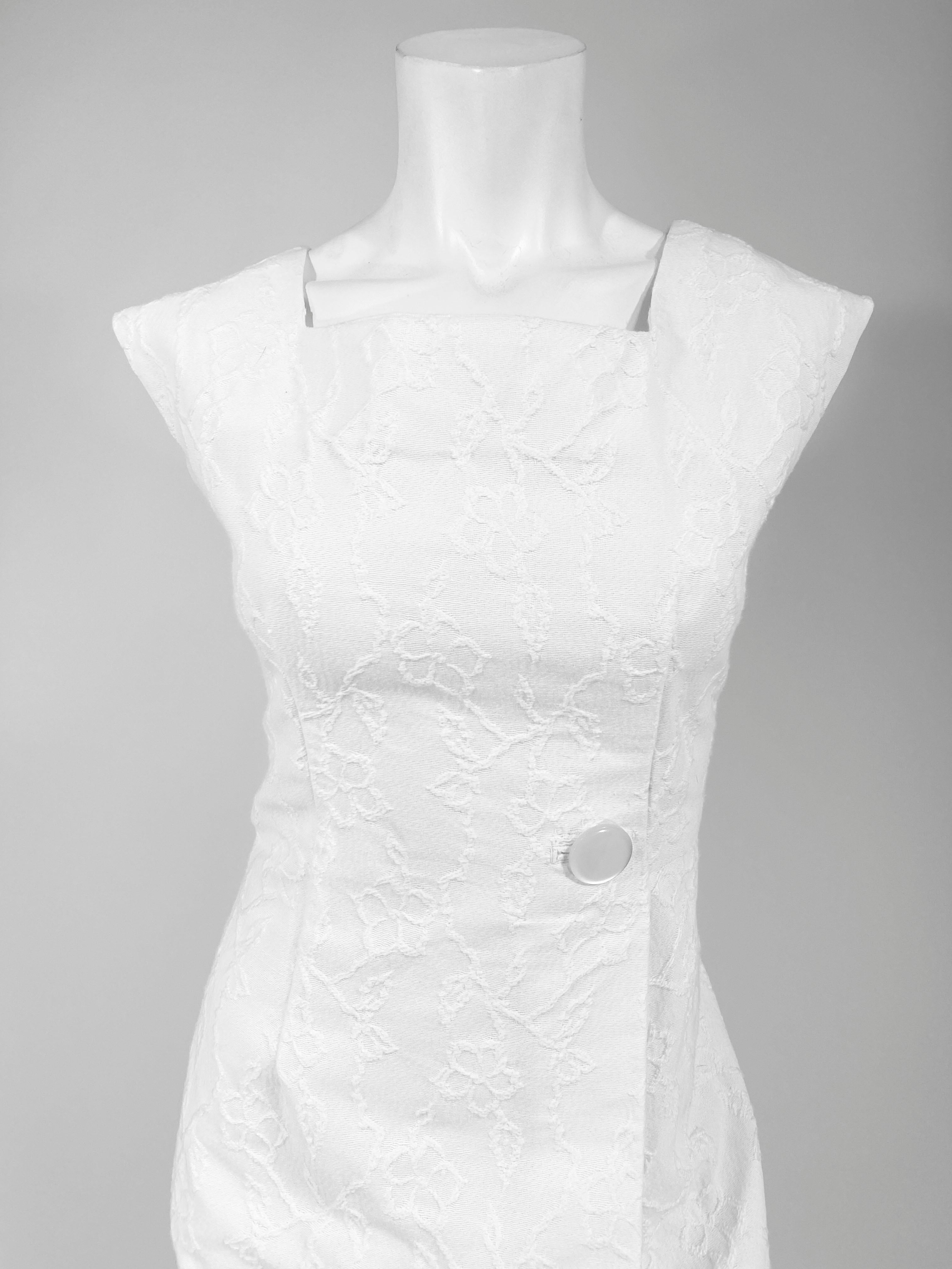 weißes Baumwoll-Jacquard-Sommercocktailkleid aus den 1960er Jahren. Rock und Mieder des Kleides sind mit einer großen, einfachen Falte anstelle einer rückwärtigen Kellerfalte versehen, die mit einem großen Knopf aus Perlmutt verziert ist. Die