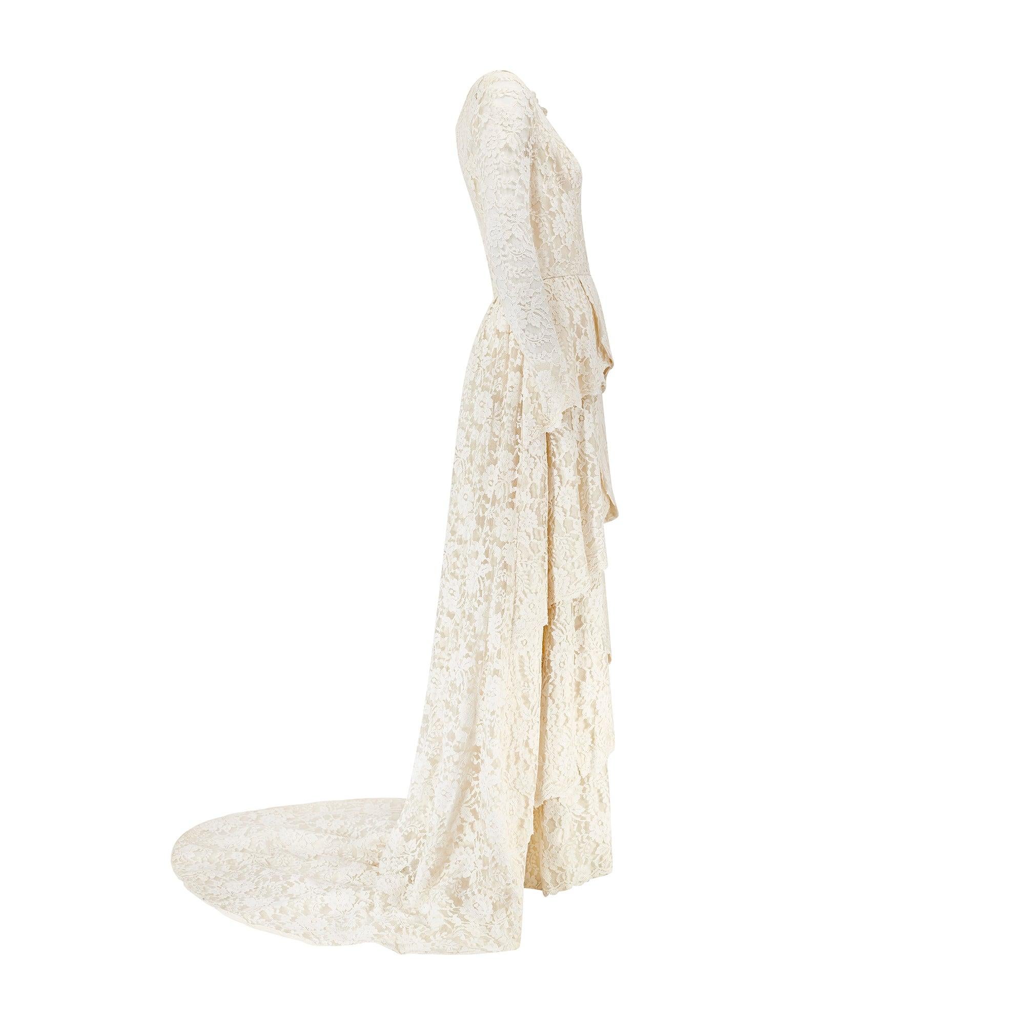 This enchanting wedding dress, with its tiered construction and layers of delicate machined lace, was created in the 1960s.  The design features a long-sleeved bodice with a fitted bust and wide, rounded neckline that reveals the décolletage. The