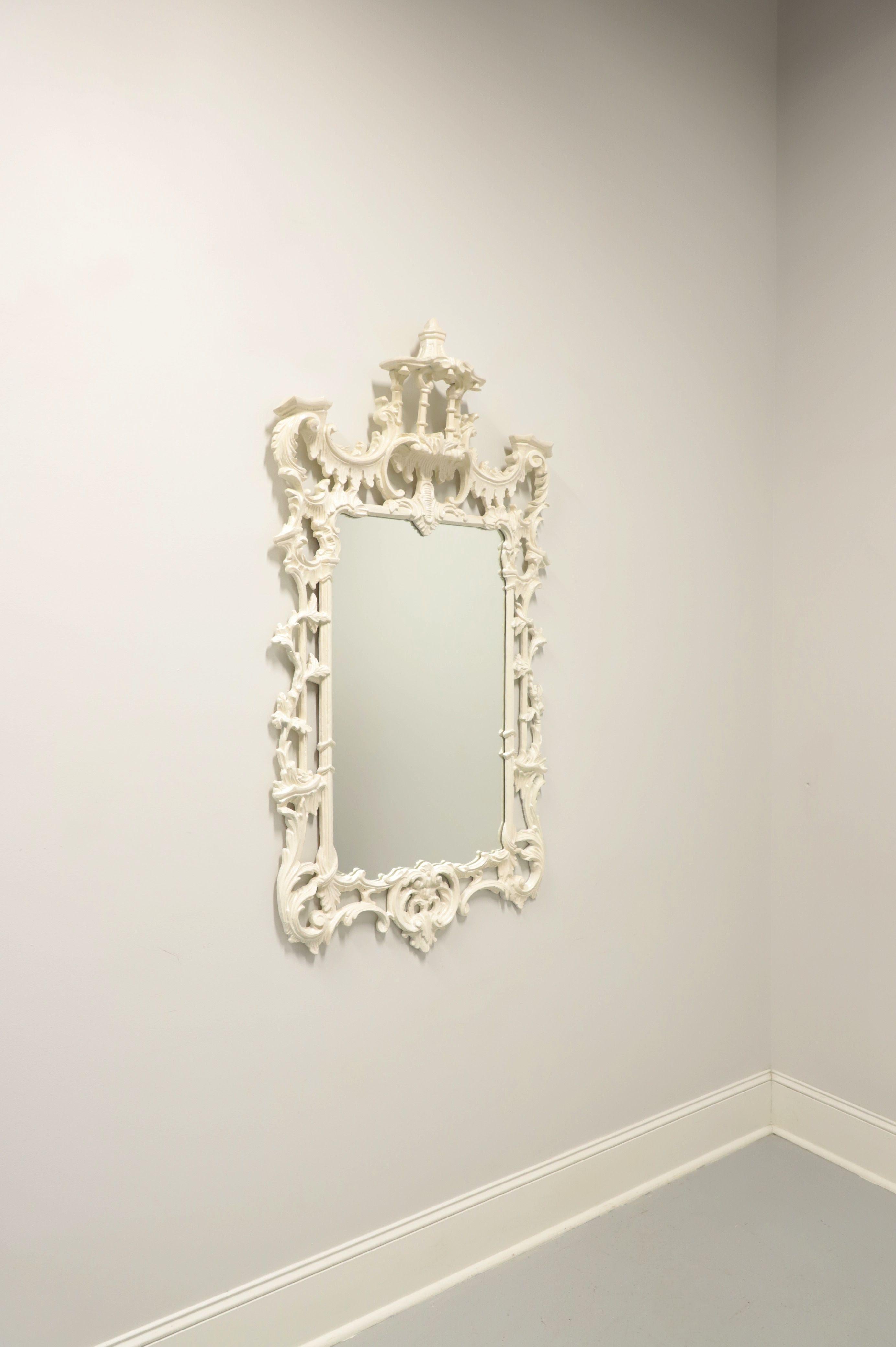 A large Chinese Chippendale style wall mirror by Stroupe Mirror Company. Mirrored glass, white lacquered solid wood frame with elaborately carved open details to top, sides and bottom. Features acanthus leaves, faux bamboo, vines and a pagoda to top