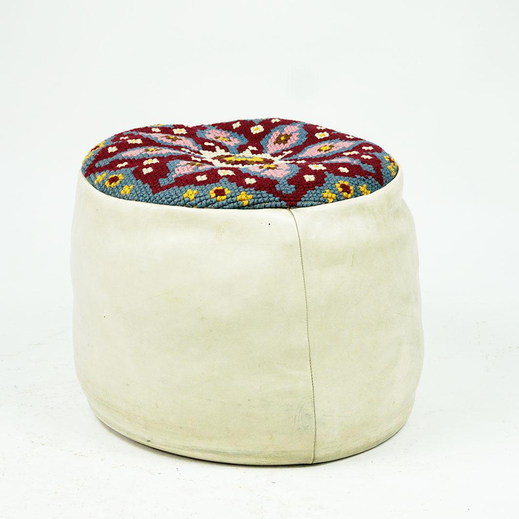 This charming white circular leather pouf has been designed and manufactured in the 1960s, probably in France. It is made of top quality white leather and has a colourful embroidered seat with yellow, white, pink, bordeaux and blue ornaments. The