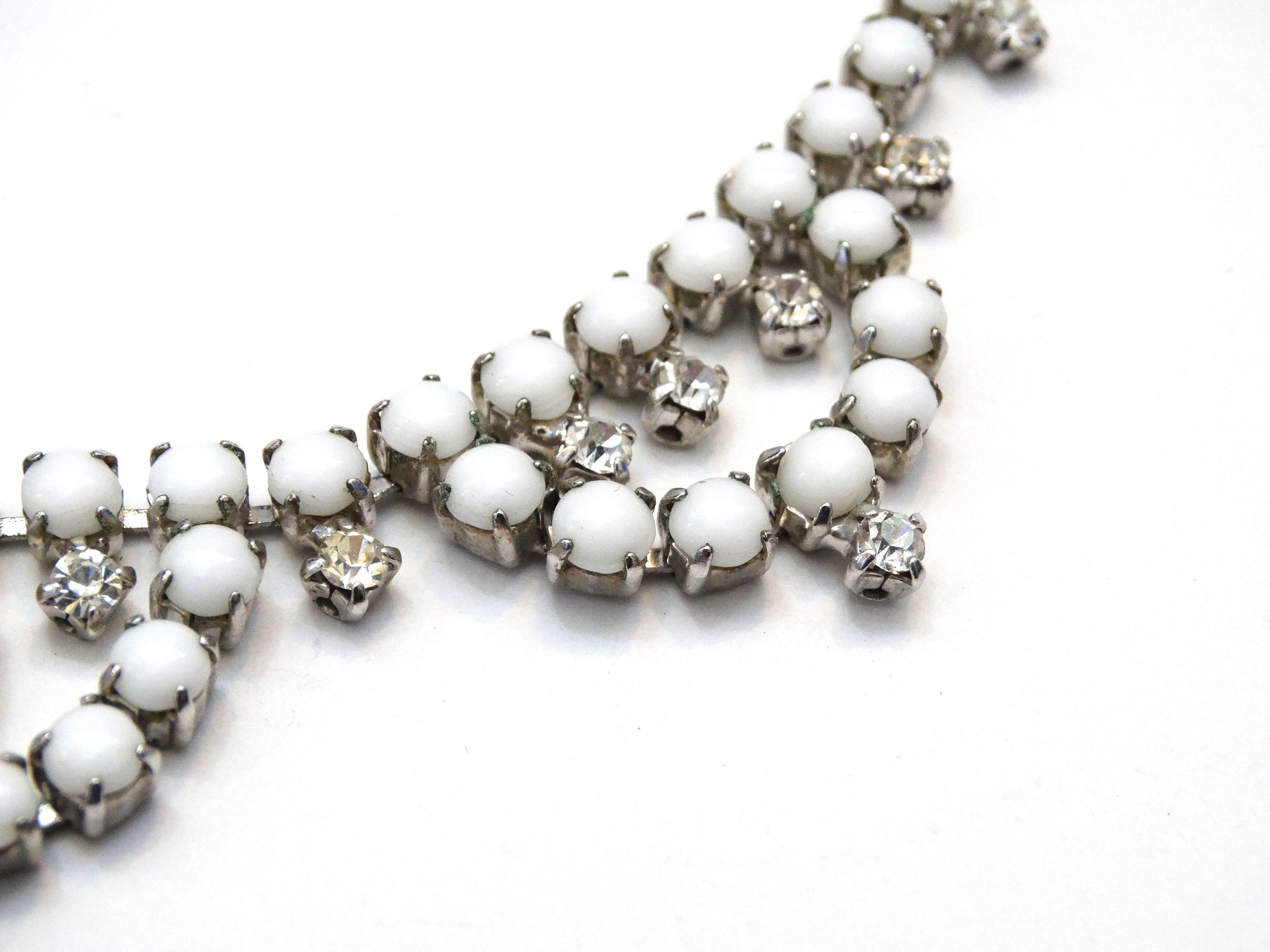 Channel the style and class of the 1960s with our amazing white rhinestone choker necklace! Milky white rhinestones contrasted with crystals throughout the piece, all set in silver toned metal. This piece has a hook closure for an adjustable fit,