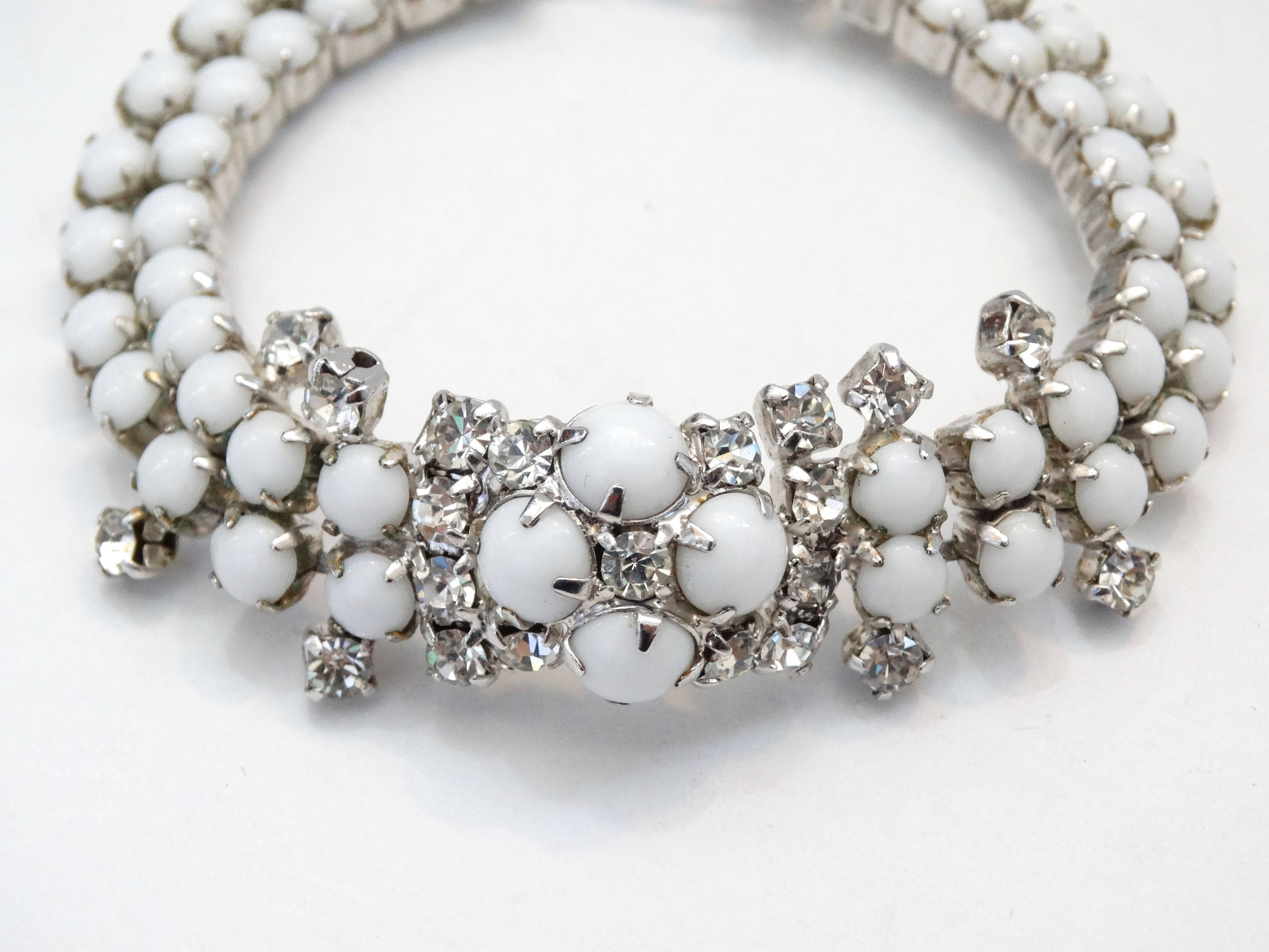 ¡La pulserita de strass con más clase de los años 60! Dos capas de brillantes de color blanco lechoso engastadas en metal plateado, acentuadas con racimos de cristales alrededor del dije central de la pulsera. El cierre se pliega y encaja en su