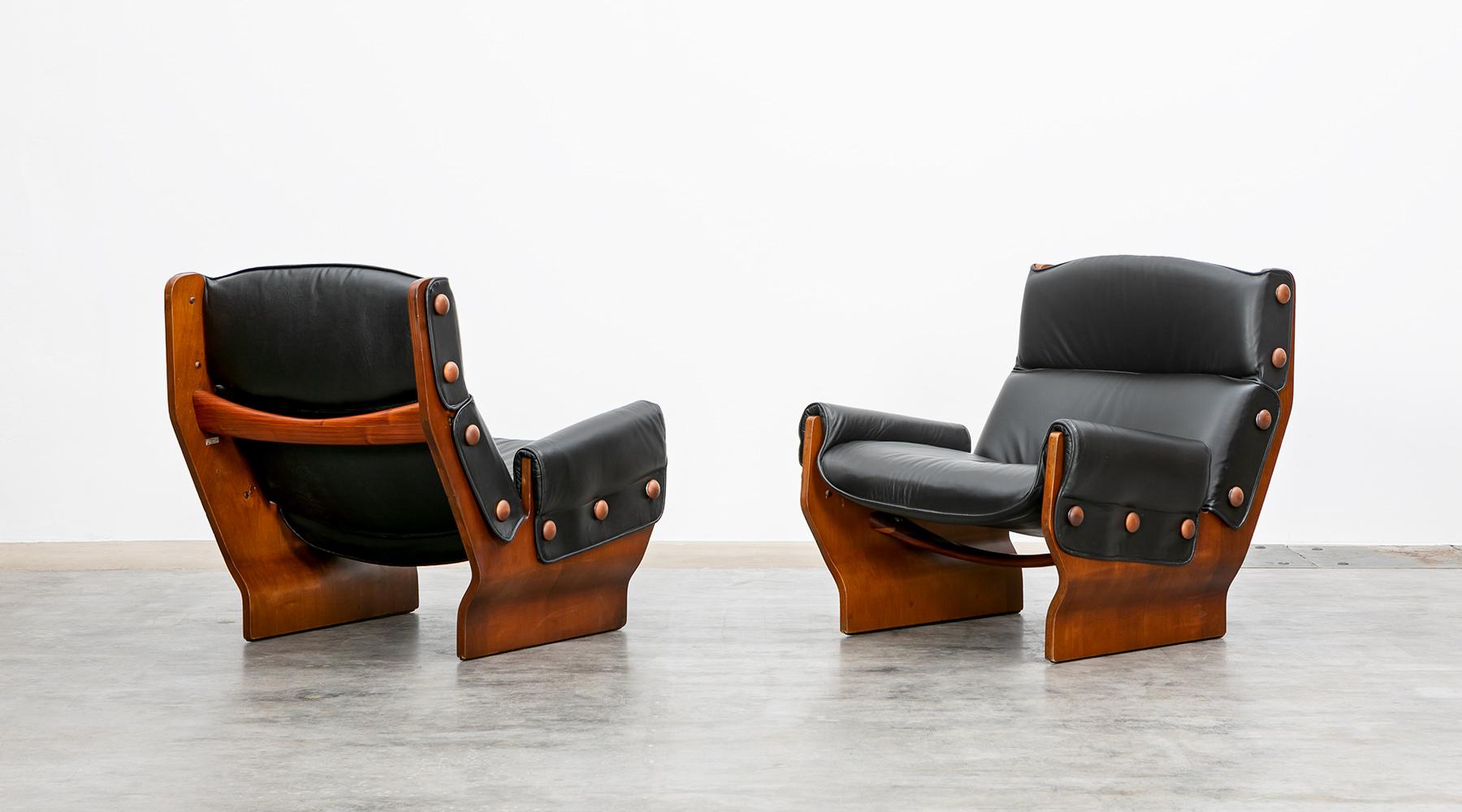 Two majestic, rustic lounge chairs designed by famous Osvaldo Borsani. The seat is made of upholstered leather and comes in good condition and sits on a wooden base. On the sides are decorative button borders, which are also made of wood. A