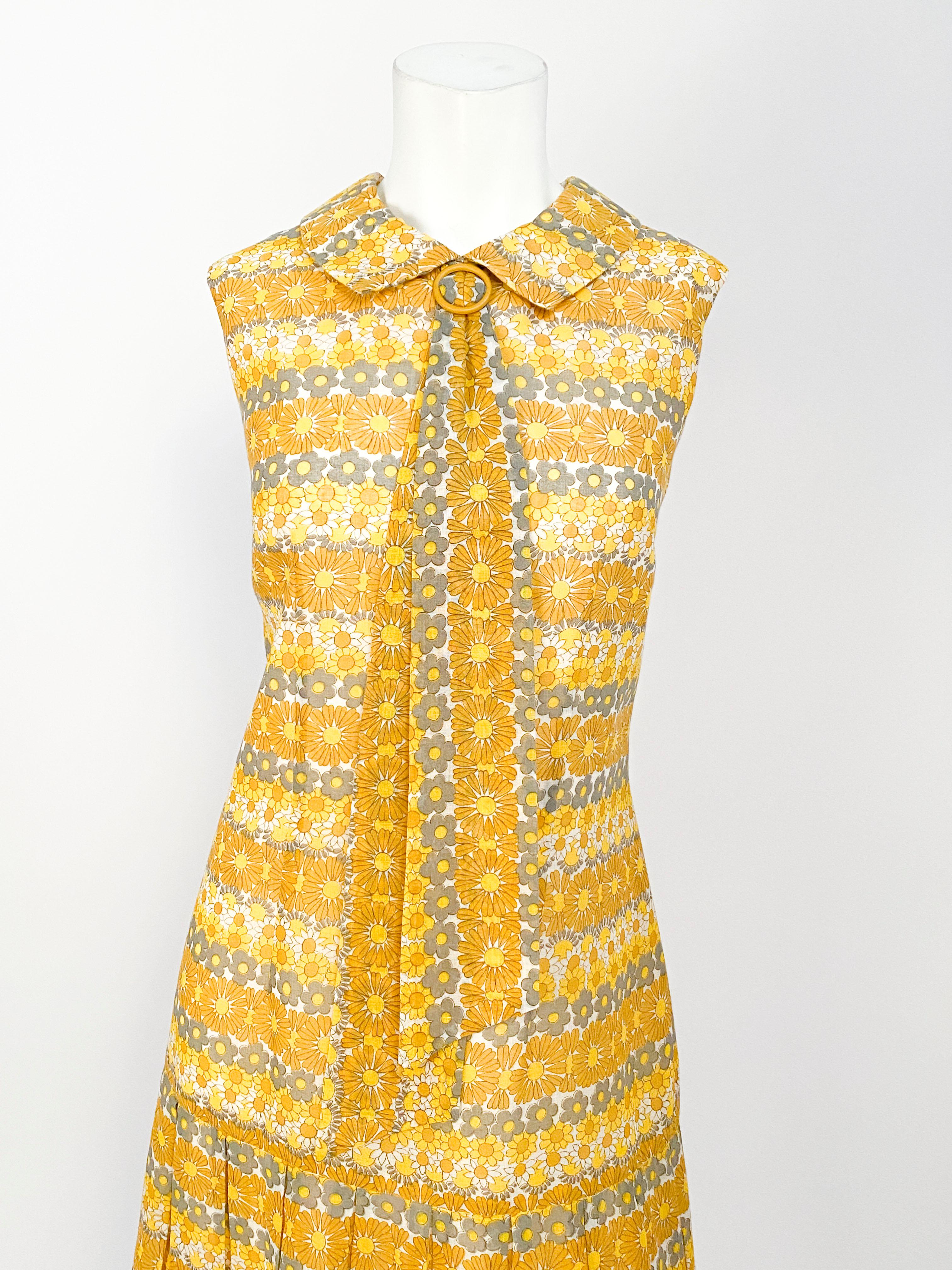 1960s yellow drop waist dress featuring a dense daisy print in tones of yellow and grey. The skirt is pleated and the peter pan collar is finished with a buckled elongated tie. 