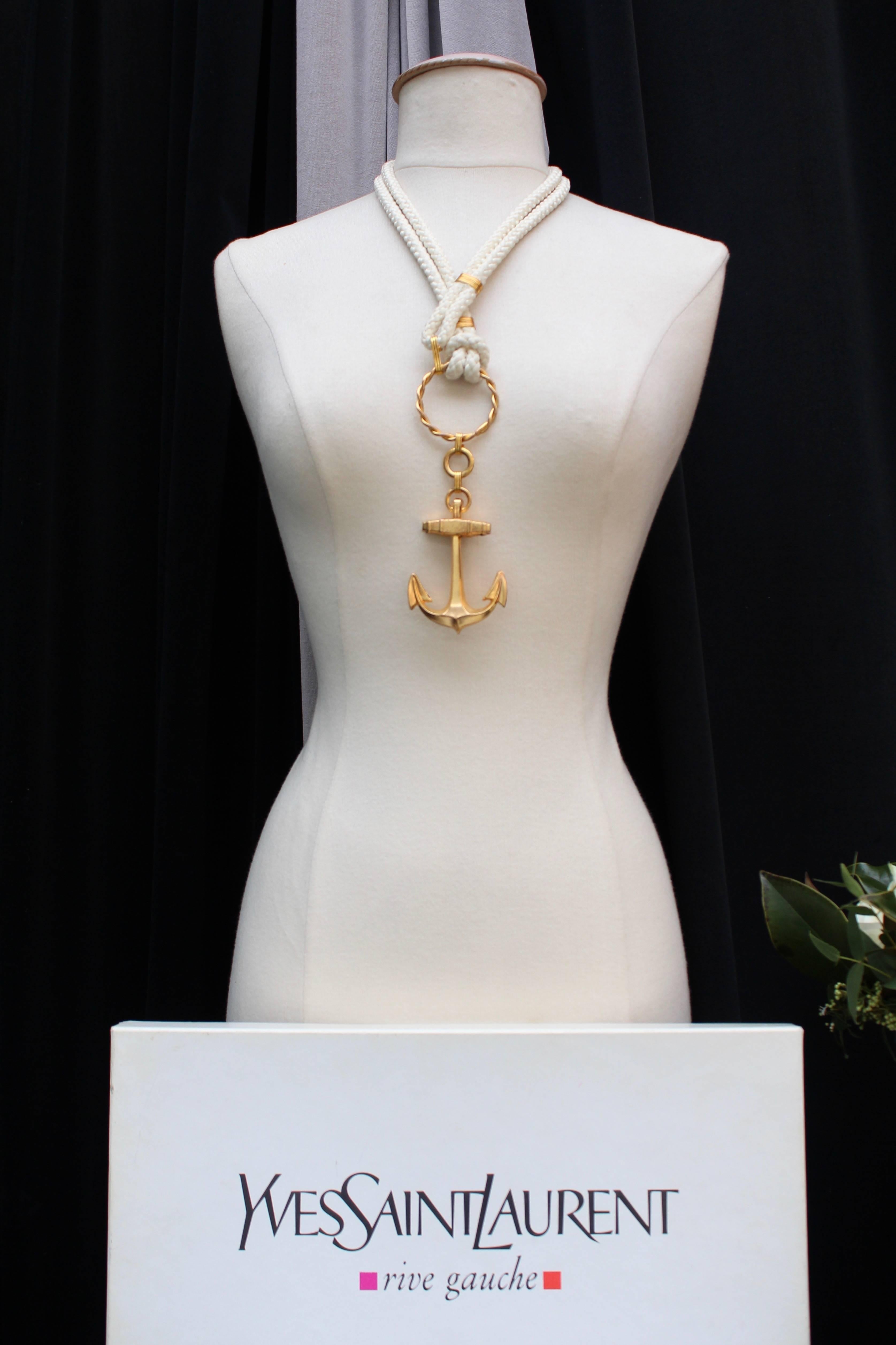 YVES SAINT LAURENT – Necklace composed of a double white cord and gilded metal hardware. It closes with a wide hook to be tied to a large or smaller ring. The necklace is embellished with a beautiful anchor, a recurring theme in Saint Laurent’s