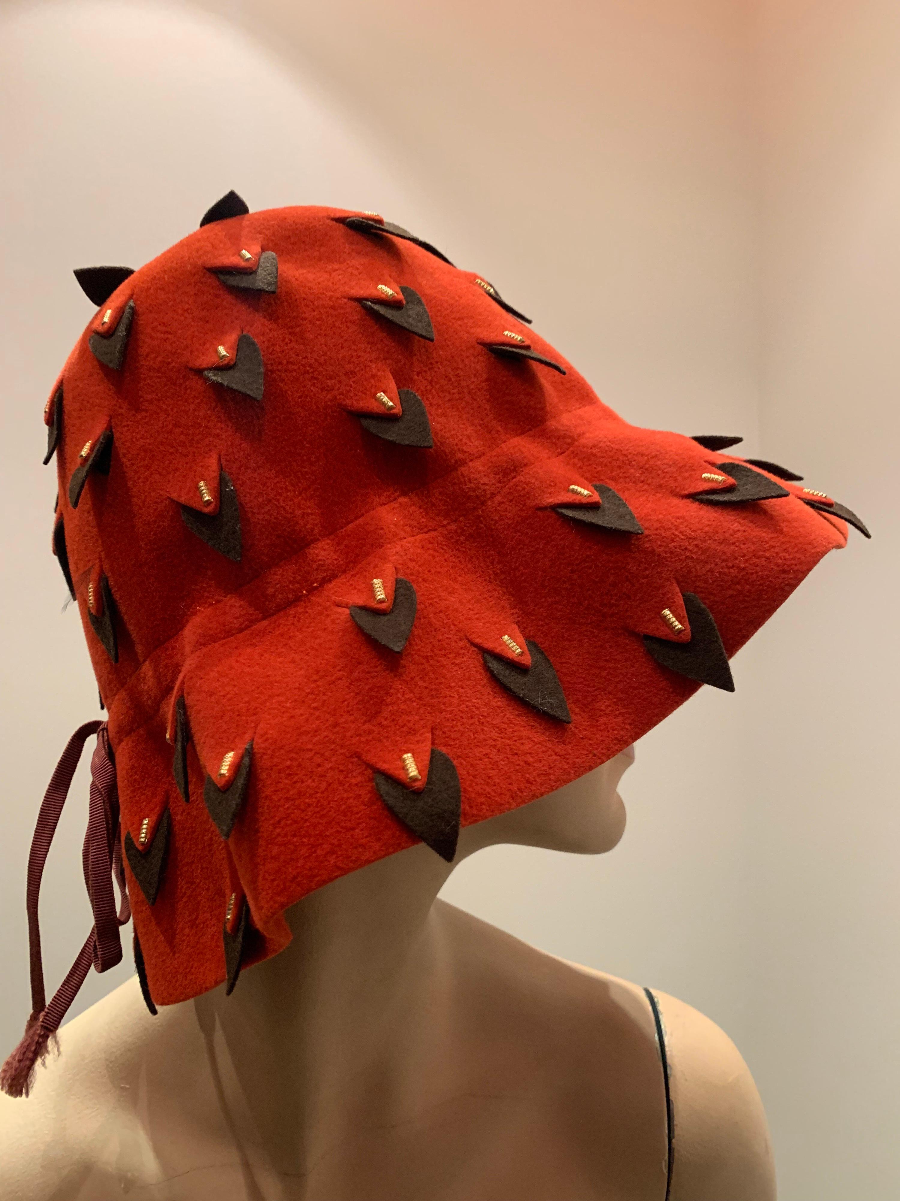 A smart 1960s Yves Saint Laurent cinnabar wool felt bucket hat with graphic black abstract vented surface cuts throughout that resemble ermine tails. A narrow black hatband is tied in a bow. Contrasting signature YSL turquoise blue grosgrain hatband