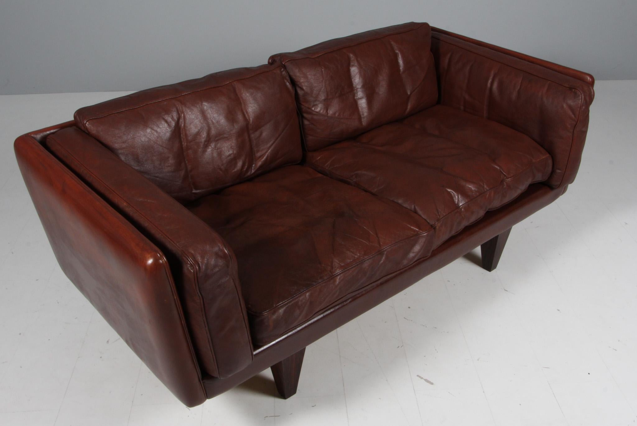 Illum Wikkelsø 1919-1999. two-seat sofa, freestanding, upholstered in brown patinated leather, loose cushions with down filling, cone-shaped rosewood legs, 1960s 1970s. Produced by Holger Kristiansen, V11 series. 
